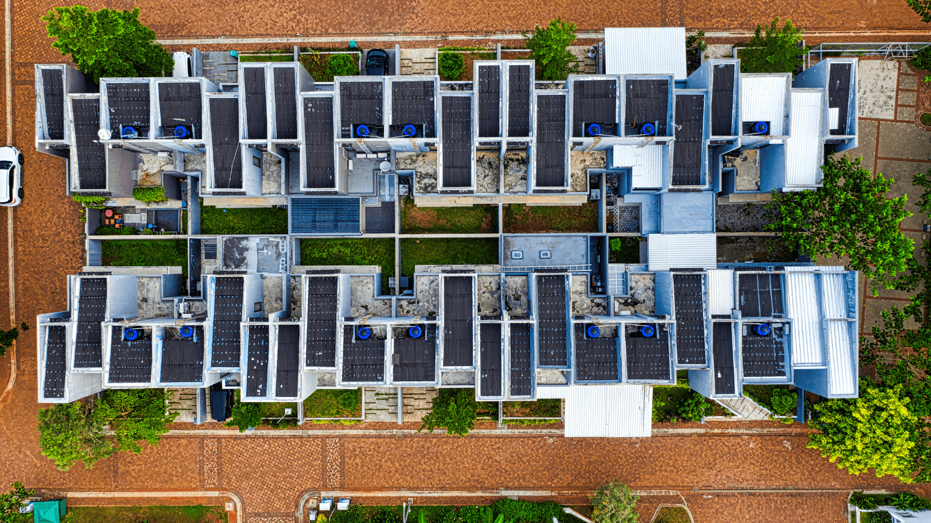 Luftaufnahme eines modernen Wohnkomplexes mit mehreren Gebäuden, auf deren Dächern Solarpaneele installiert sind.