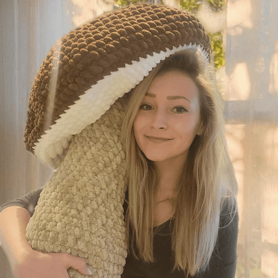 A person wearing round glasses, a yellow beanie, and a yellow t-shirt stands smiling against a vibrant yellow background.