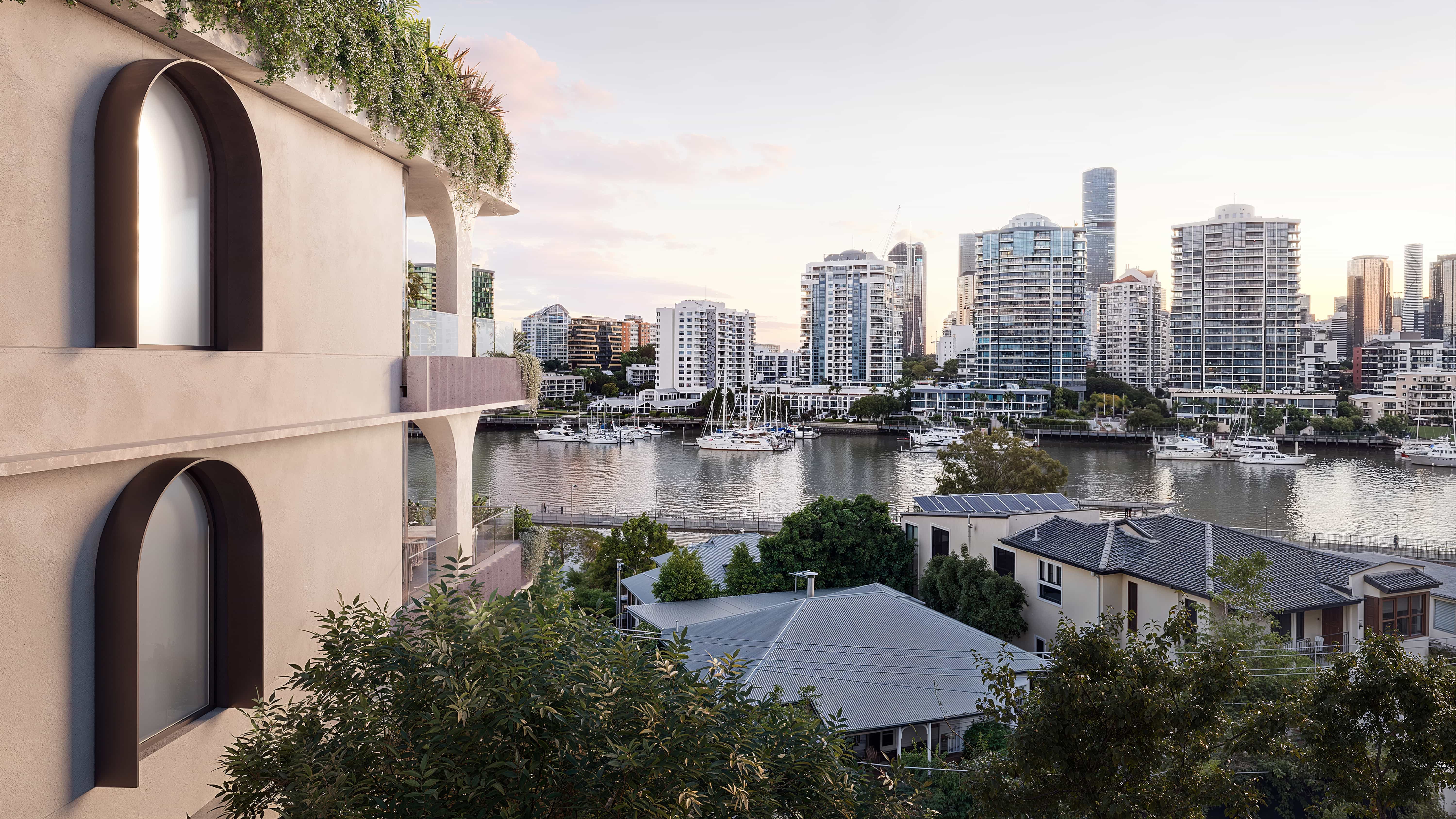 Luxury apartment balcony with outdoor dining and panoramic views of the city skyline and river, showcasing sculptural concrete design and greenery.