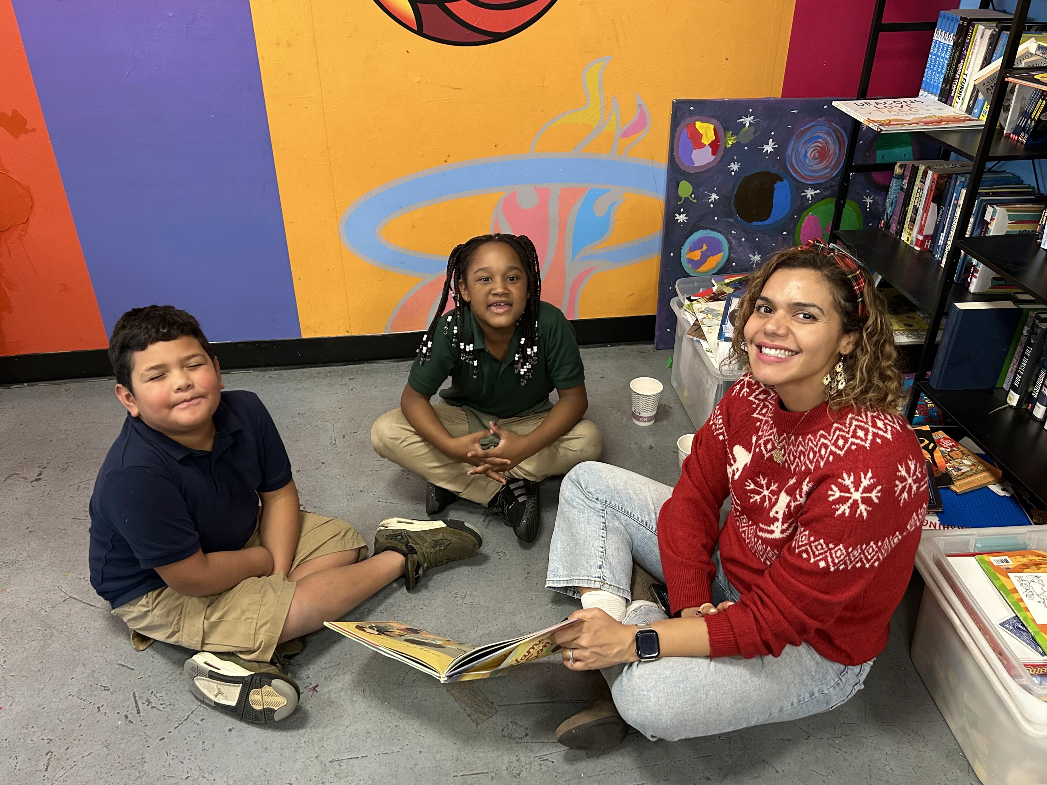 A volunteer reading with two young people during a campus holiday gathering