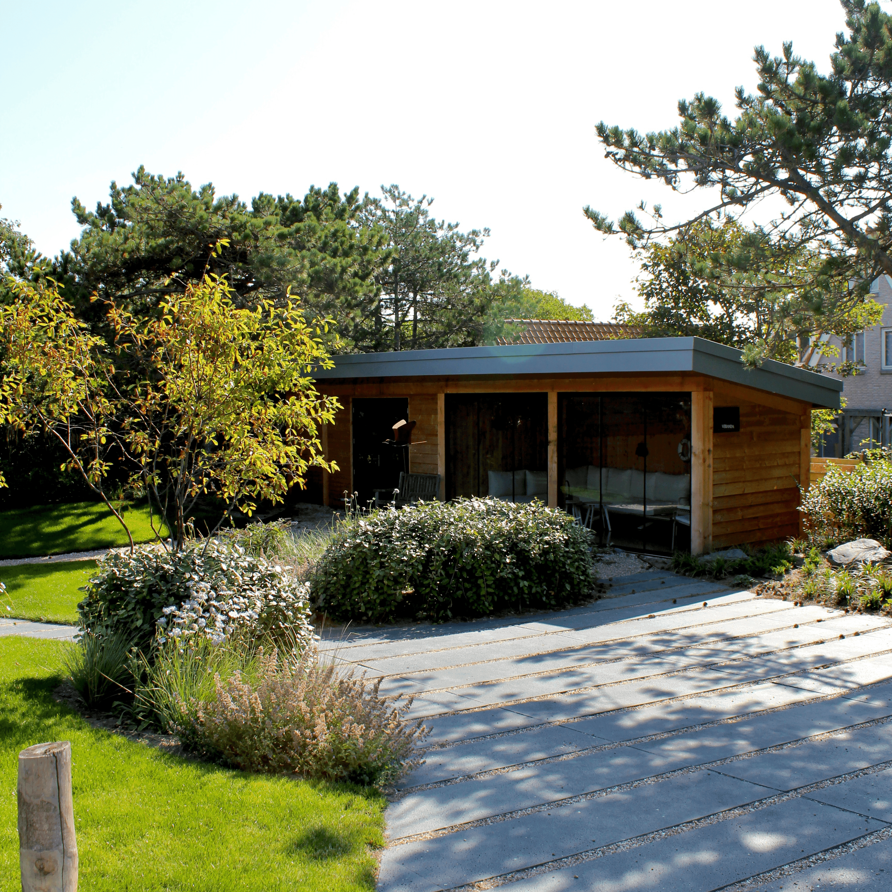Spacious modern apartment with a kitchen island, black chairs, and stainless steel appliances. A cozy living area with armchairs and plants in the background.