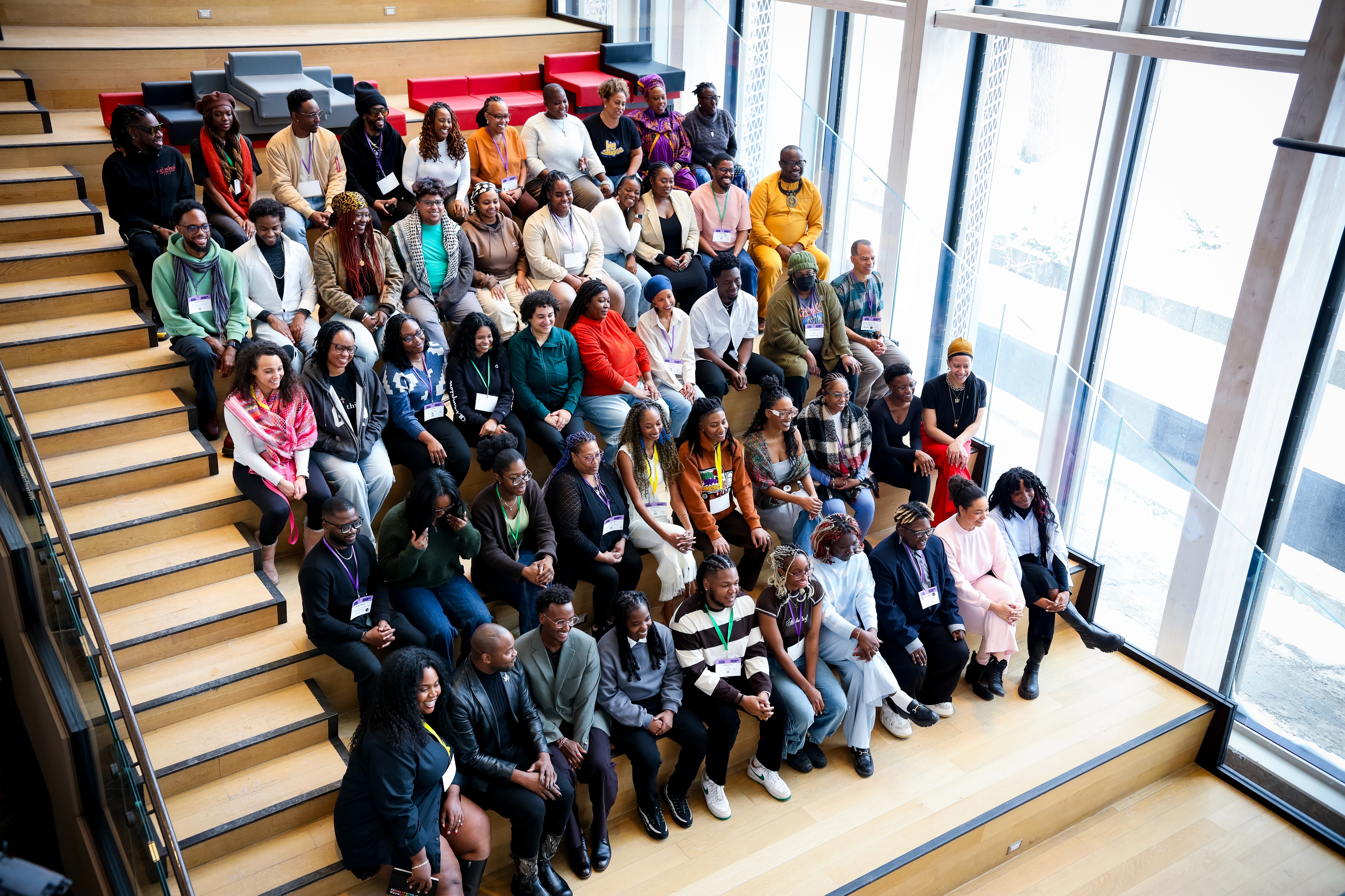 A diverse group of people sitting together on steps in a spacious, well-lit area, engaged in a gathering.