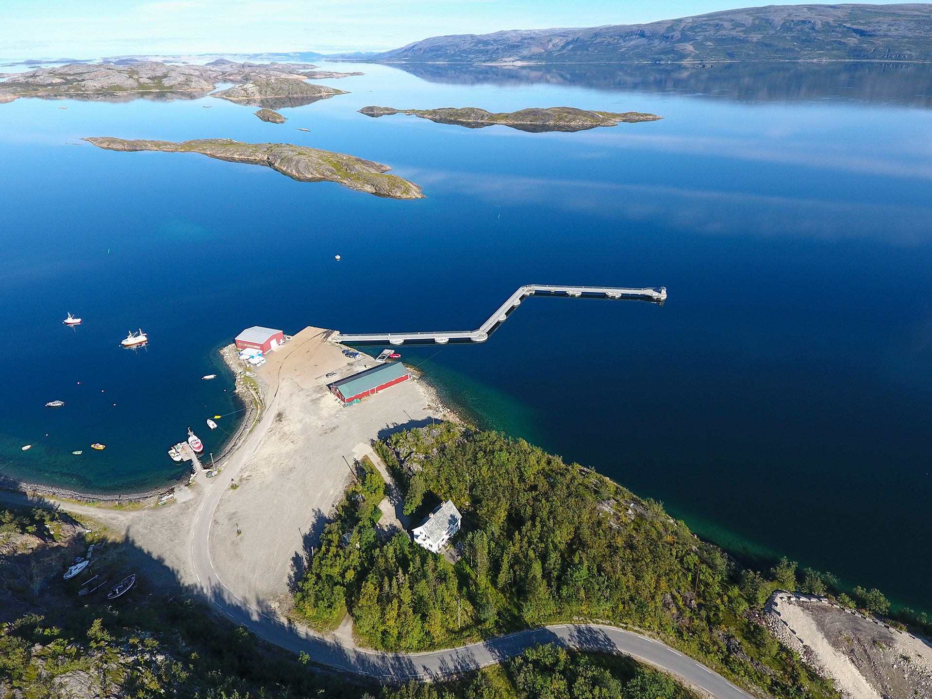 Aerial view of a floating pier extending from shore at Lakselv, Norway, providing cruise and passenger access across calm fjord waters.