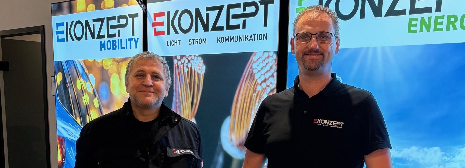 Zwei Männer posieren vor einem Ekonzept-Banner, E-Mobility, Licht, Strom, Kommunikation
