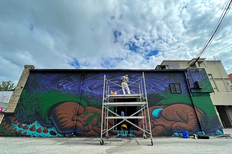 A painter on scaffolding against a sky of cloud, purple and green spreading across the long wall.