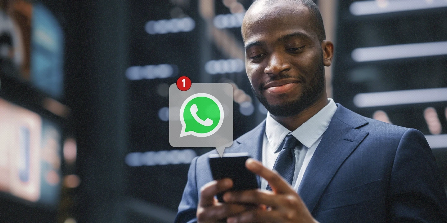 Empresário feliz, vestido de terno, olhando para o celular enquanto recebe uma notificação do WhatsApp