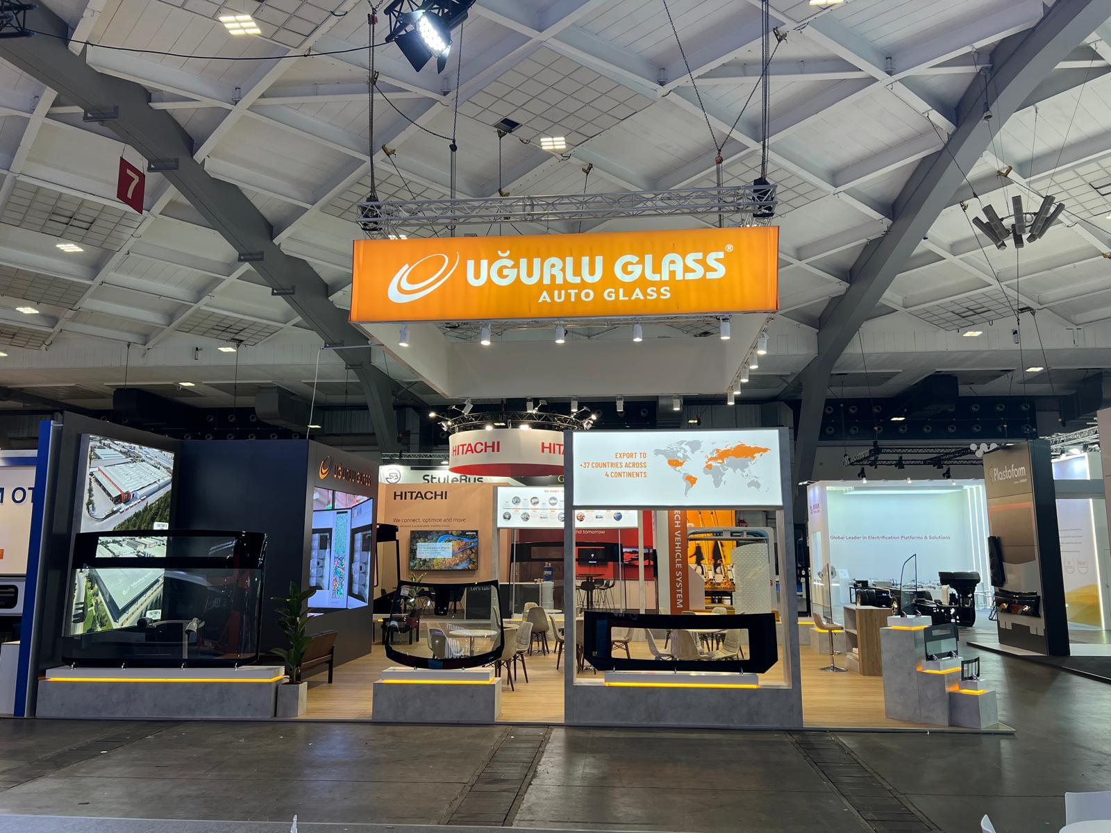 Large illuminated orange hanging sign above the Uğurlu Glass stand, providing long‑distance visibility and strong brand presence.