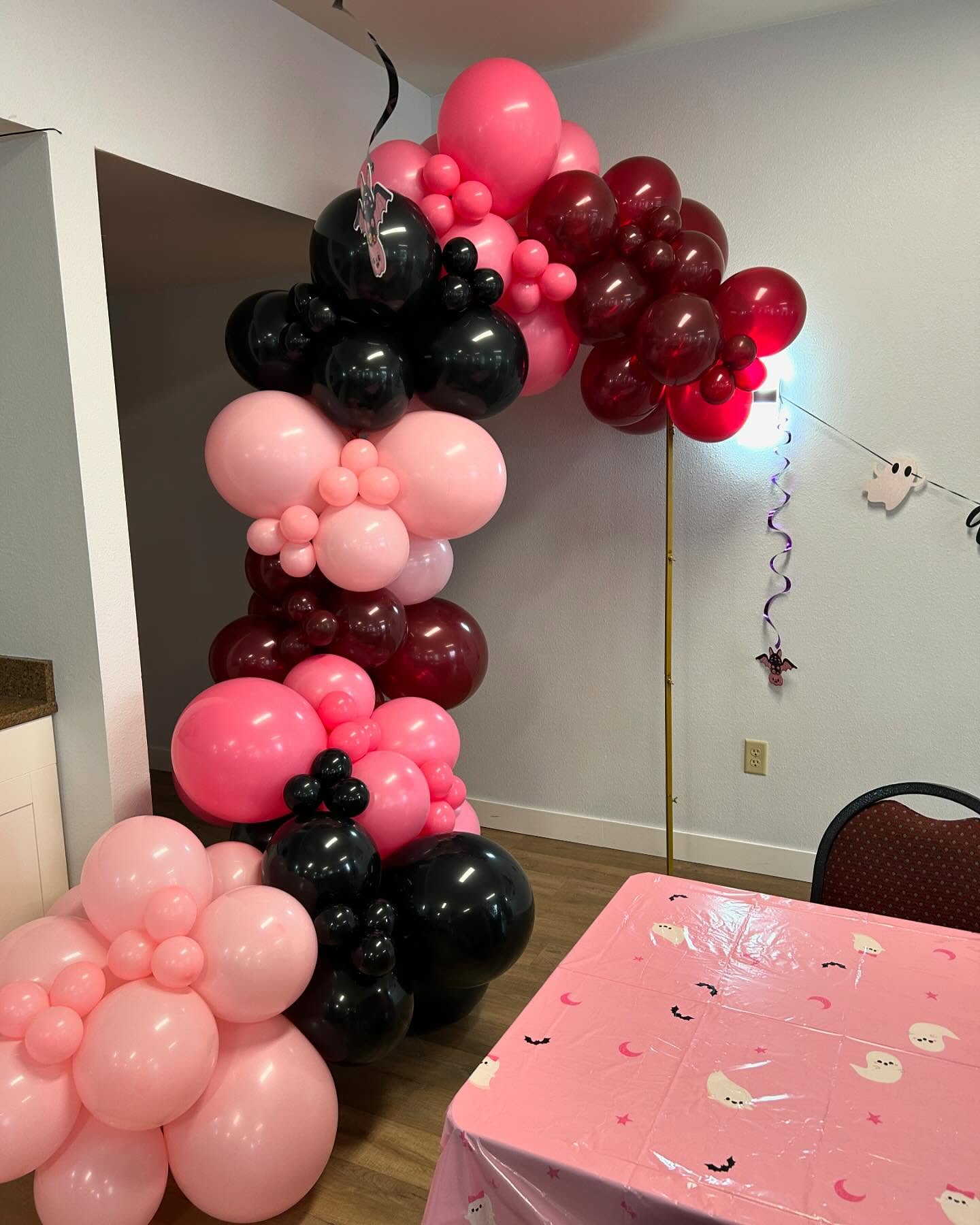 Pink, black, and red balloon arch framing a party table decorated with matching colors created by Be Bold Balloons