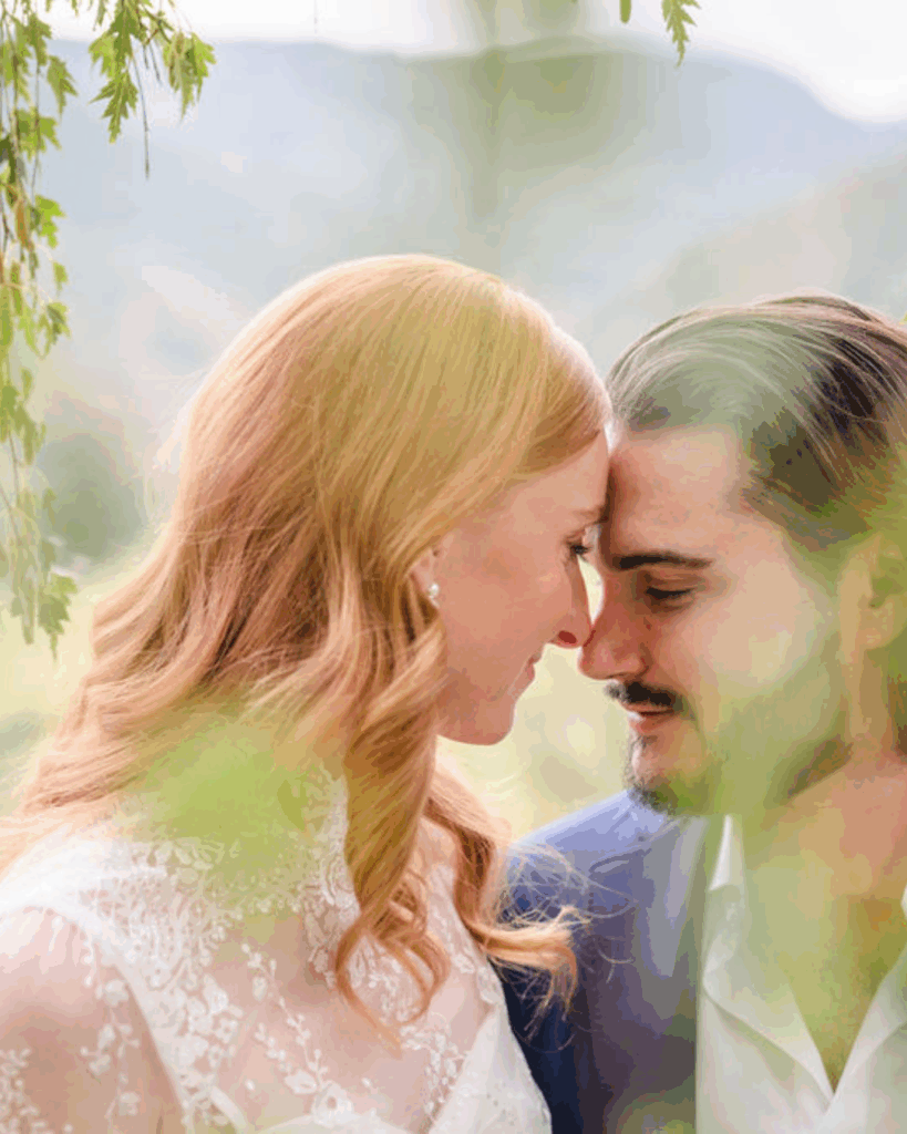 Newlyweds touching foreheads, framed by green leaves