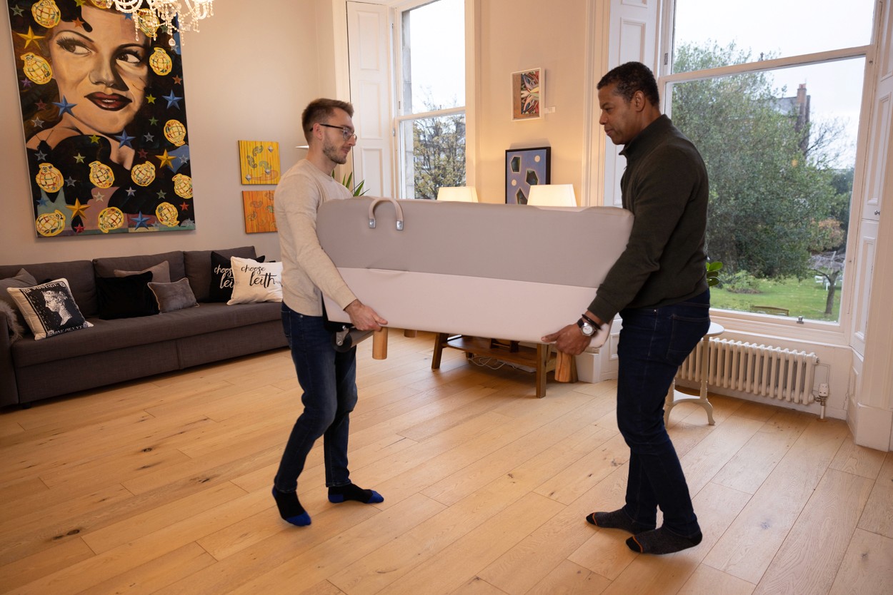 Two people lifting the BackHug device together, demonstrating the recommended method for moving or placing it down.