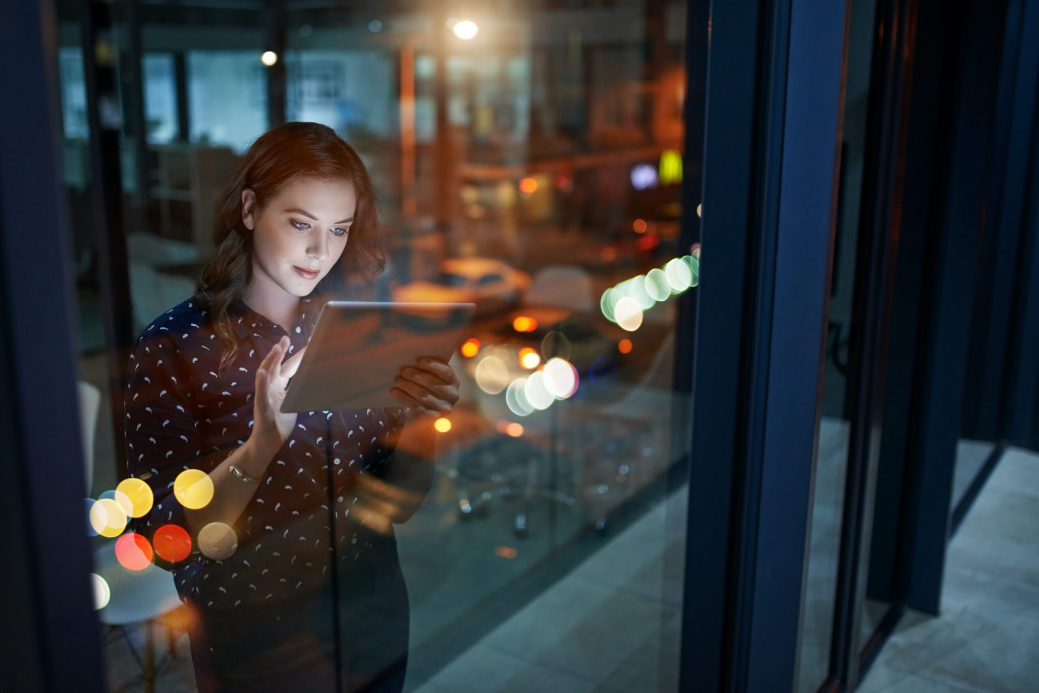 Woman using tablet by office window at night