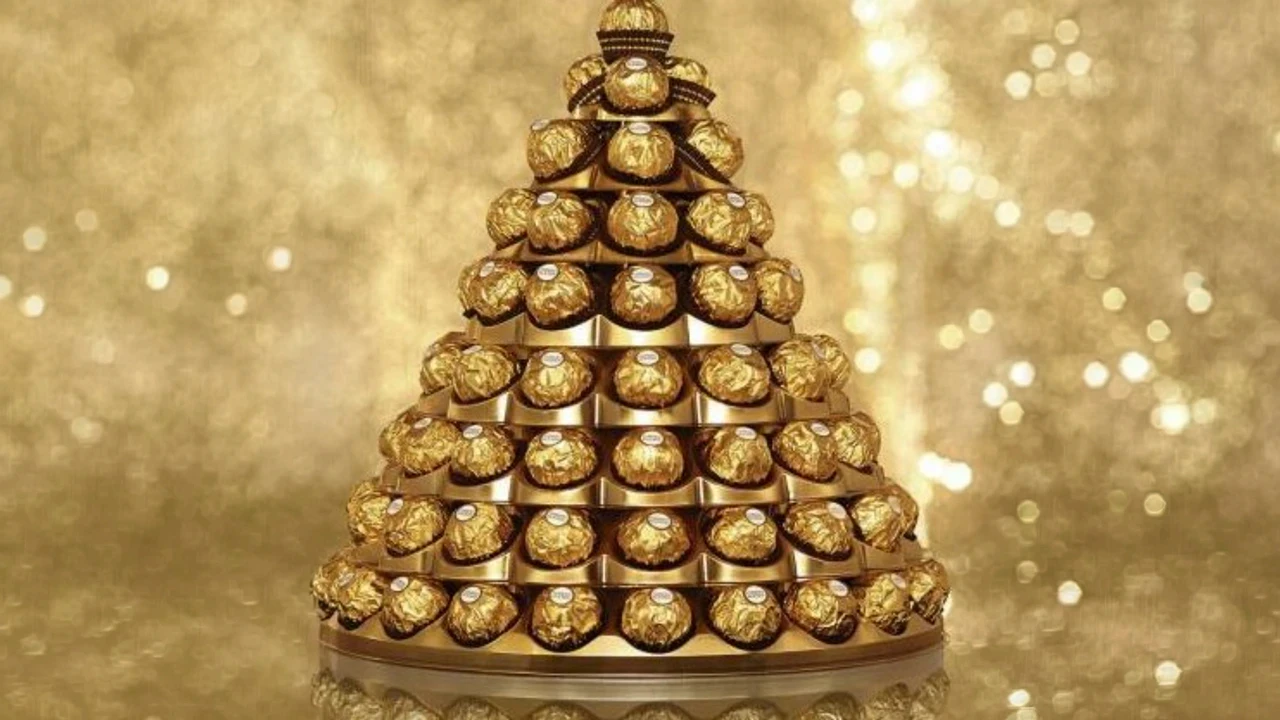 Structure pyramidale composée de nombreux chocolats emballés dans un papier doré, soigneusement empilés sur un présentoir circulaire. L’ensemble forme une silhouette de sapin sur un fond scintillant aux tons or. Chaque chocolat est visible individuellement tout en participant à l’harmonie de la composition. Cette image accompagne la thématique “Transformez vos salariés en ambassadeurs”, en symbolisant la mise en valeur de chaque collaborateur pour construire une marque employeur forte, cohérente et rayonnante.