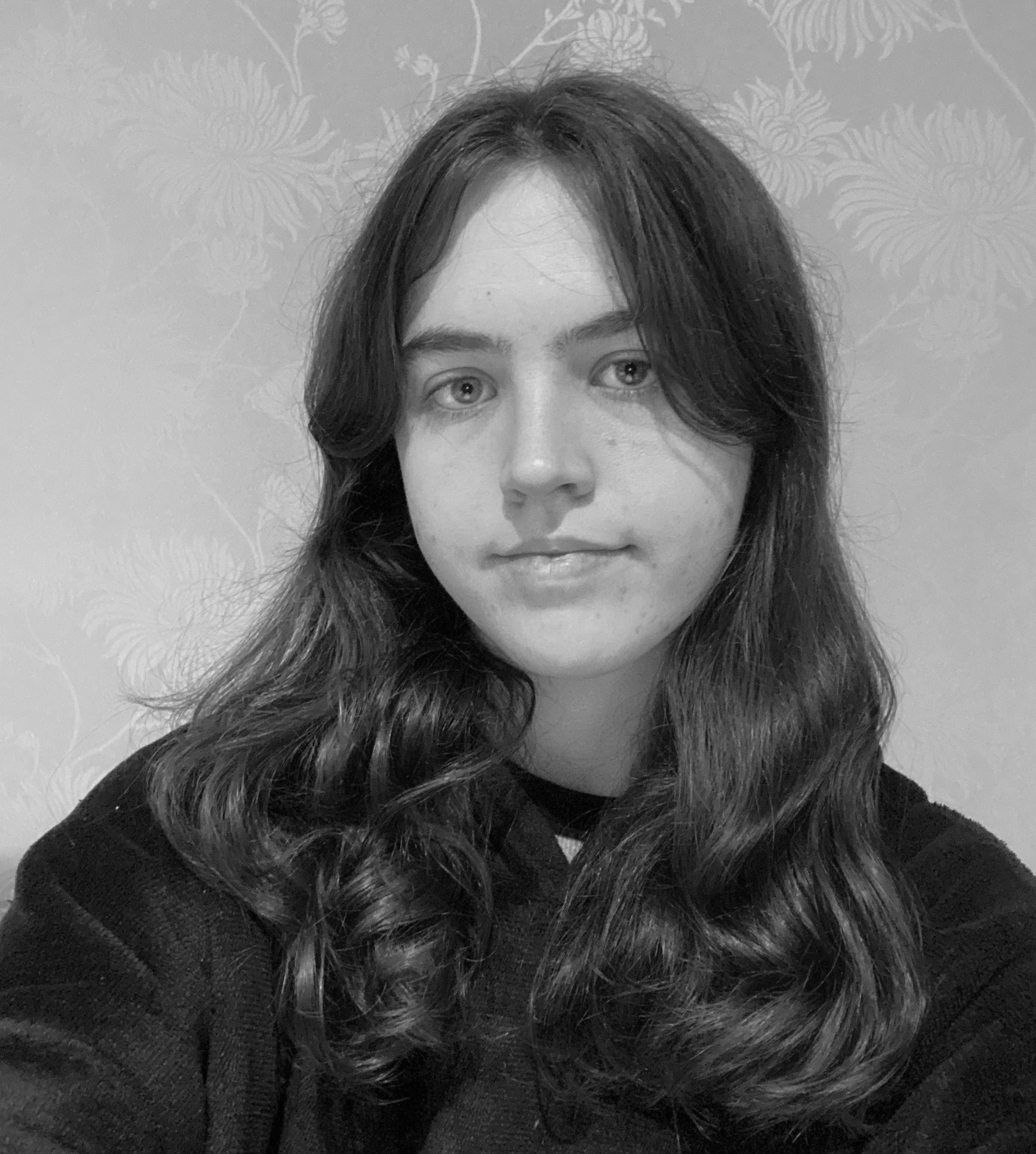 A thoughtful young person with dark hair gazes to the side, captured in soft black and white lighting.