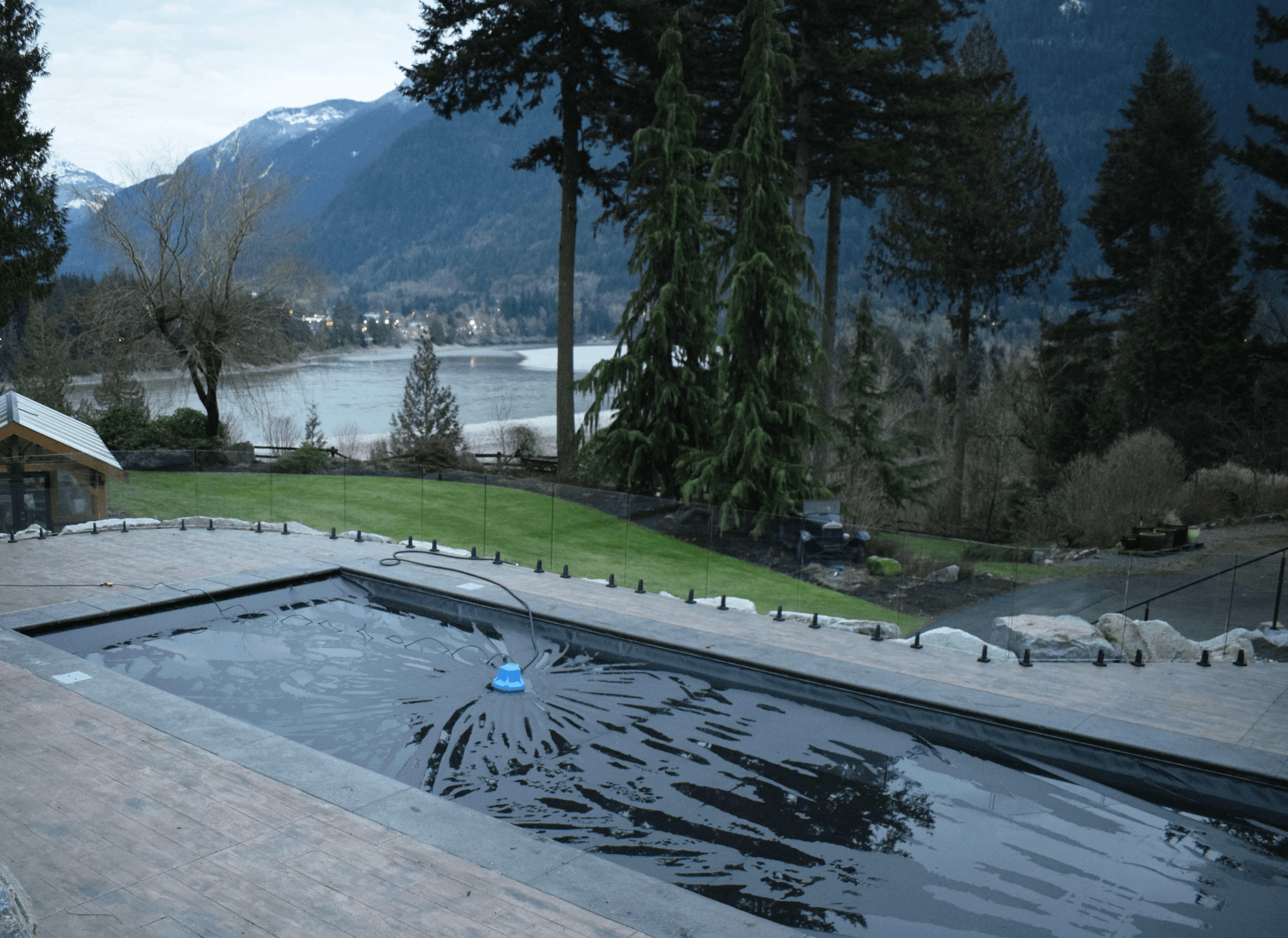 Modern cedar deck with frameless glass railings and black mounting hardware overlooking a forested lakeside mountain view. Exposed old-growth timber construction and warm cedar soffits create a clean west coast contemporary design.