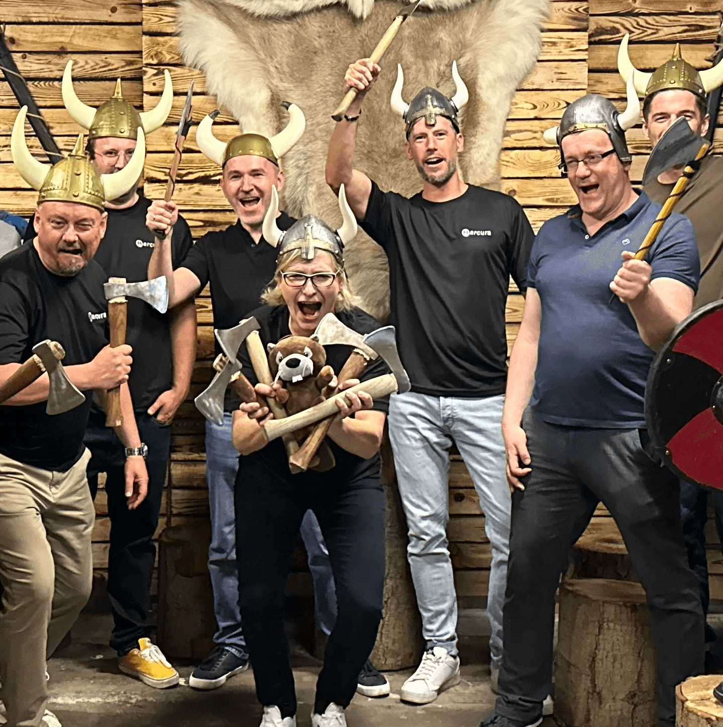 A group of eight people smiling and celebrating, holding props and wearing novelty hats in a festive setting.