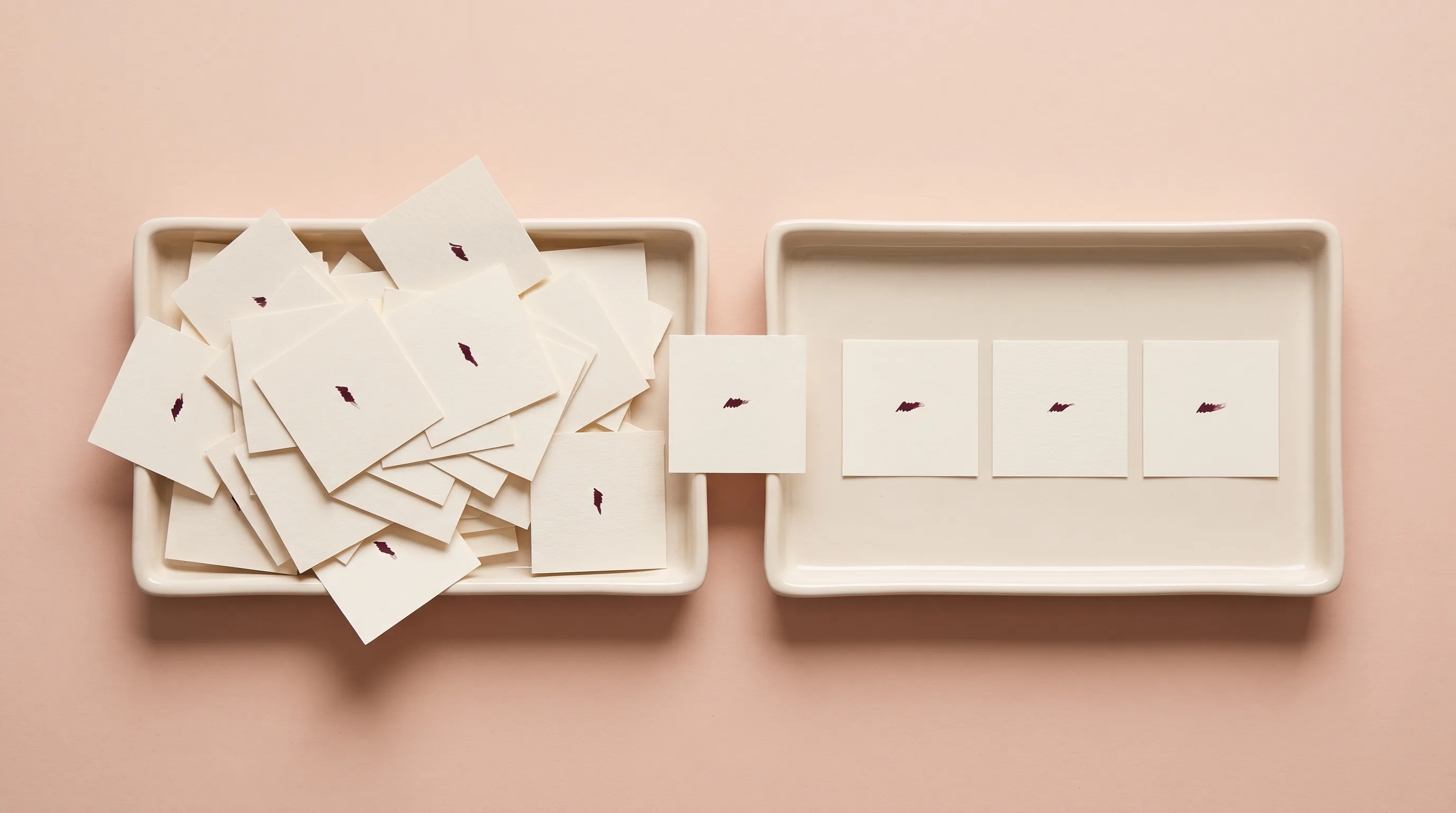 Two trays side by side, one heaped with disordered paper slips and one holding three laid flat, with a single slip in transit between them