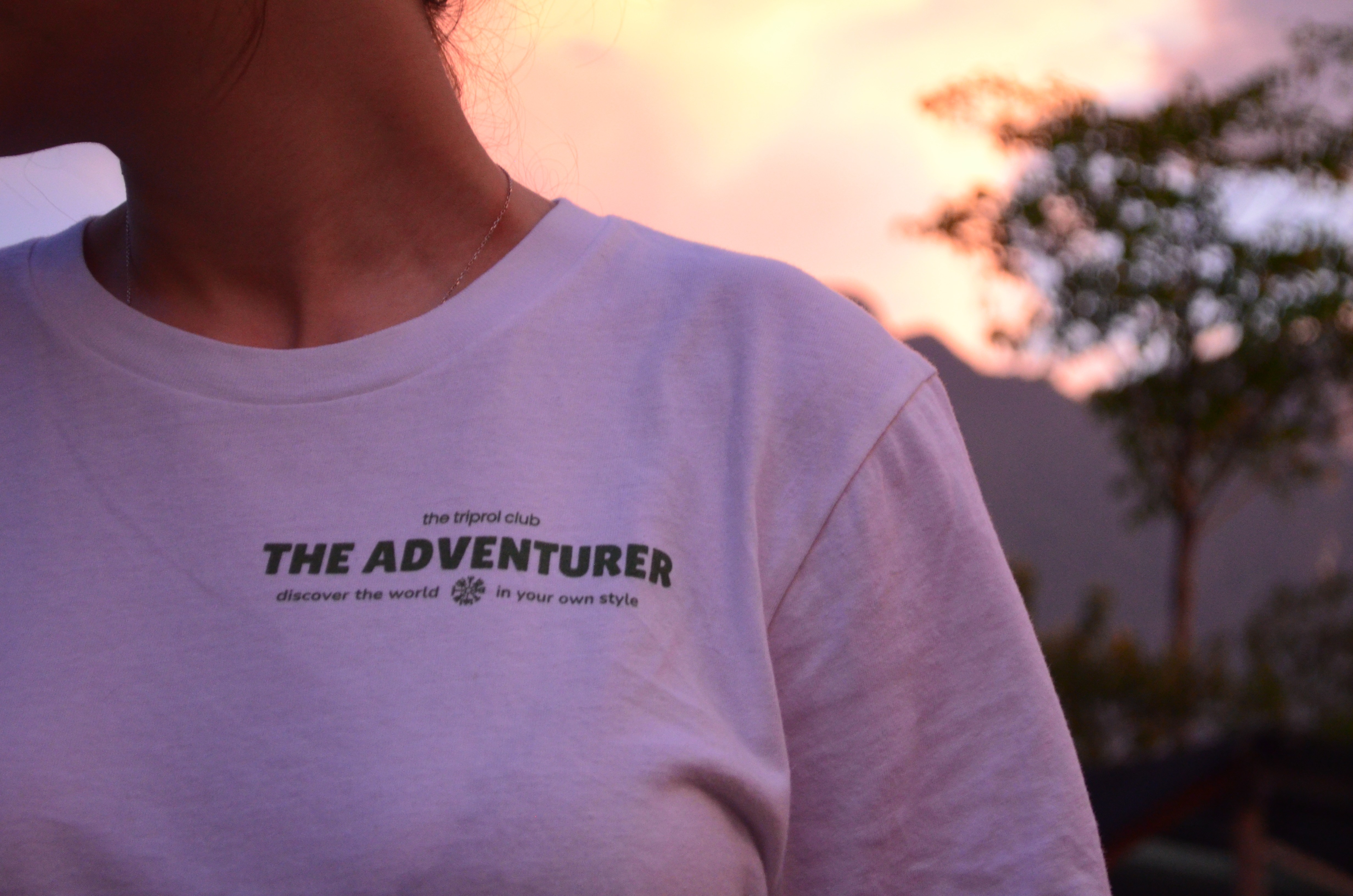 Smiling young woman with long hair standing against a dark green background, holding a finger to her chin.
