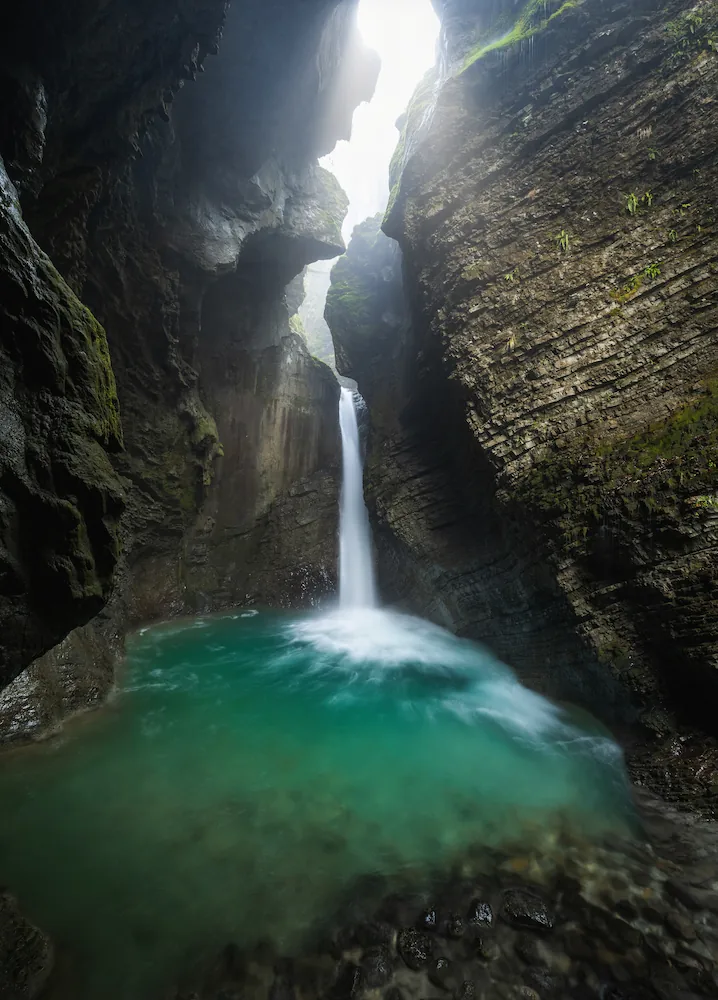 Kozjak Waterfall cascading into a deep emerald pool inside a dramatic, rocky cavern near Kobarid, Slovenia.