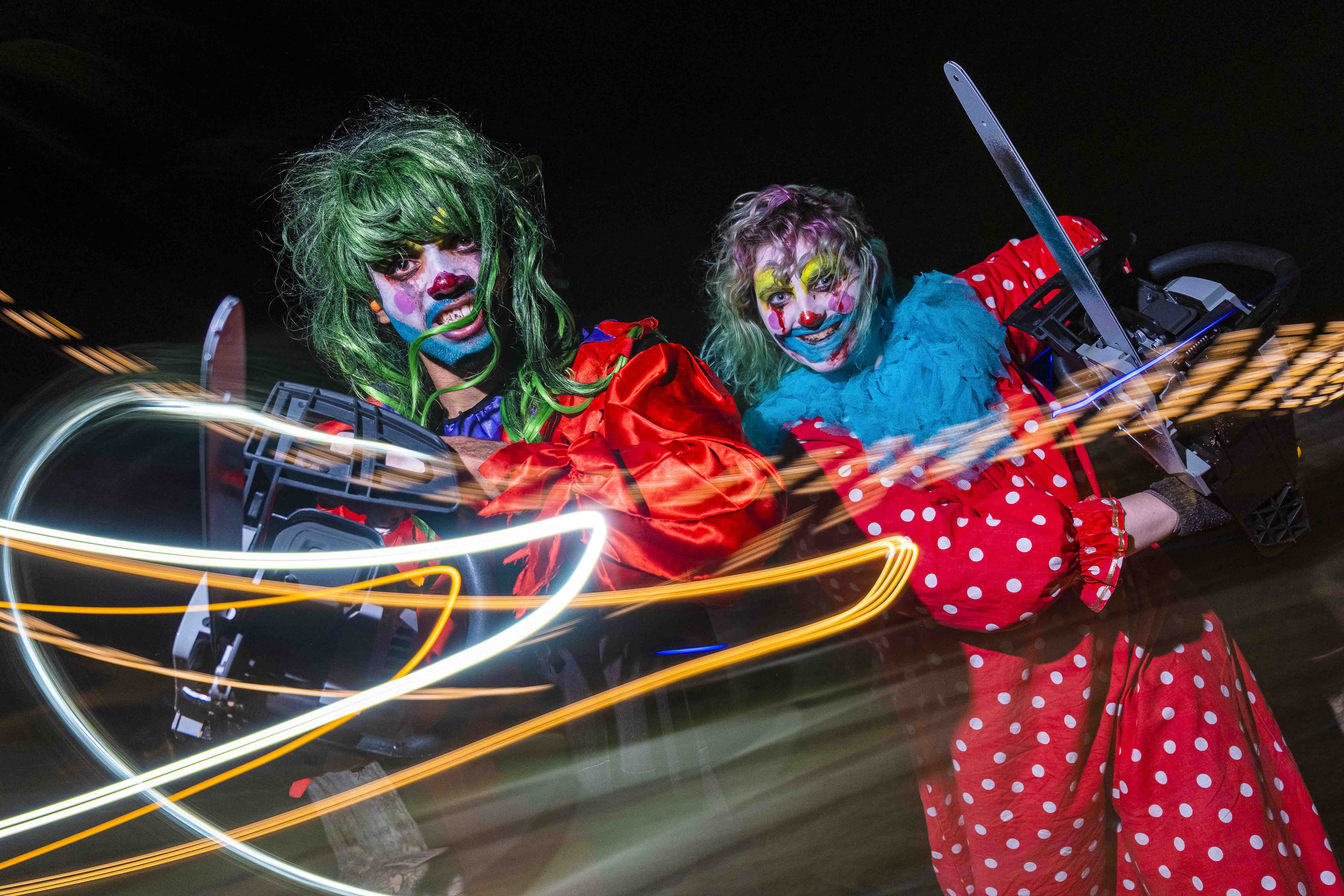 Eerie clowns with vivid face paint and colorful costumes hold chainsaws, with dynamic light trails creating a dramatic, unsettling atmosphere.