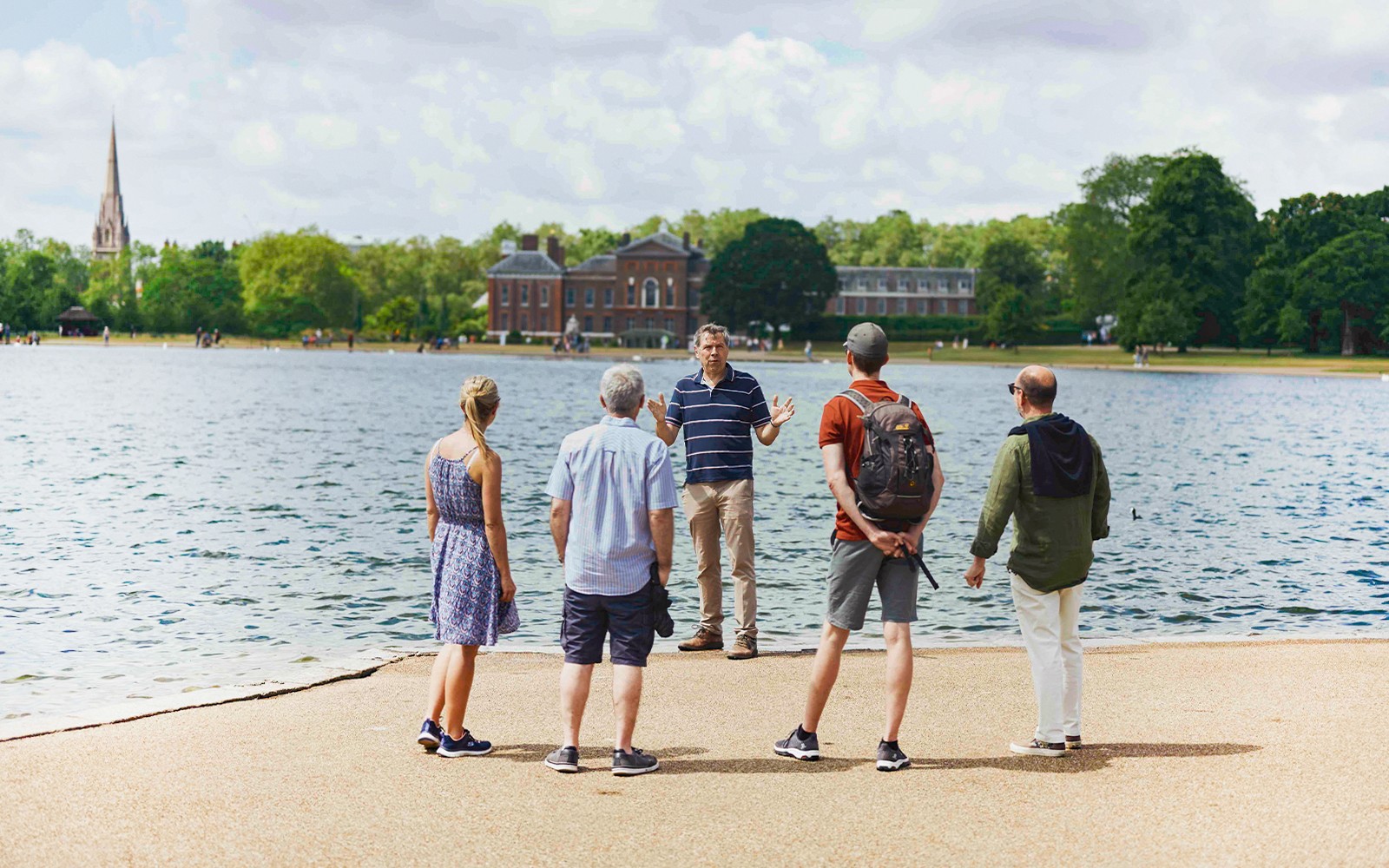 Tour group by Kensington Palace lake, listening to a guide during the Royal Afternoon Tea experience.