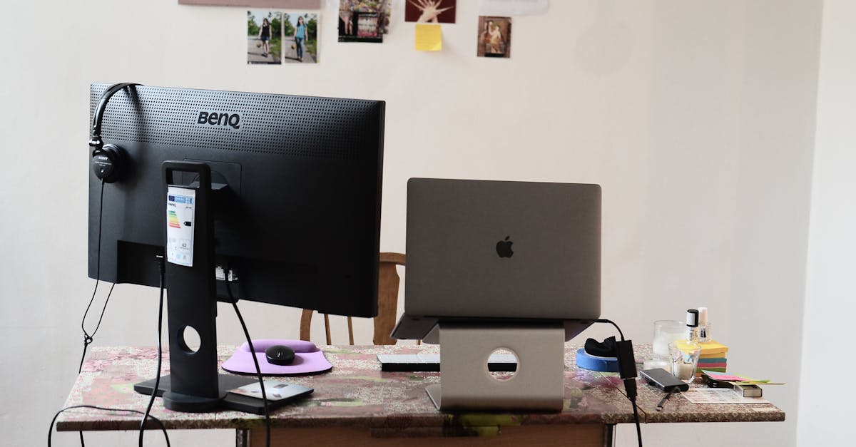 Black monitor with headphones placed on desk with modern netbook on stand against wall with photos a