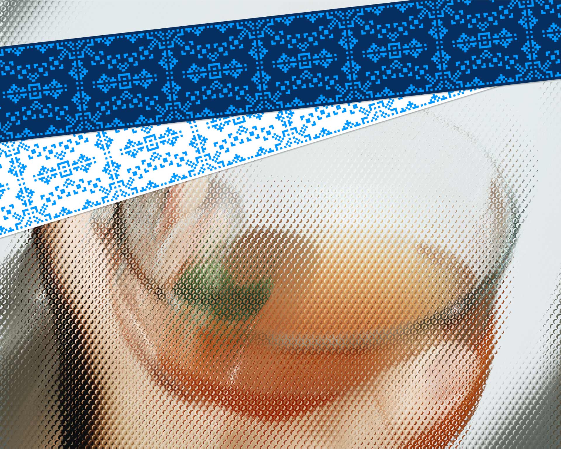 A hand holds a clear glass filled with an amber-colored cocktail adorned with a small mint leaf, contrasted against a patterned blue and white tablecloth.