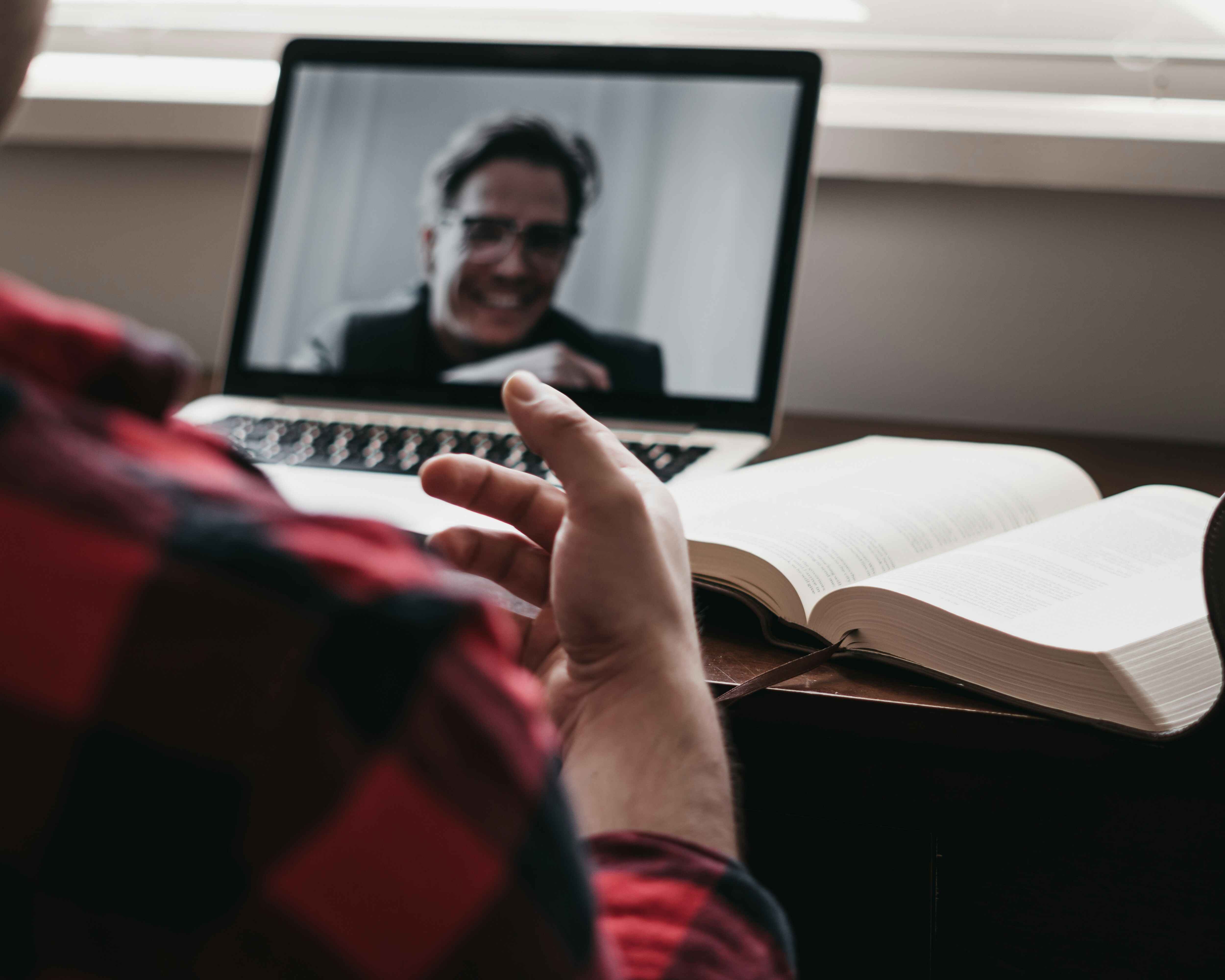 A man sits at a desk with a laptop and an open book, engaged in online therapy at the Family Time Center.