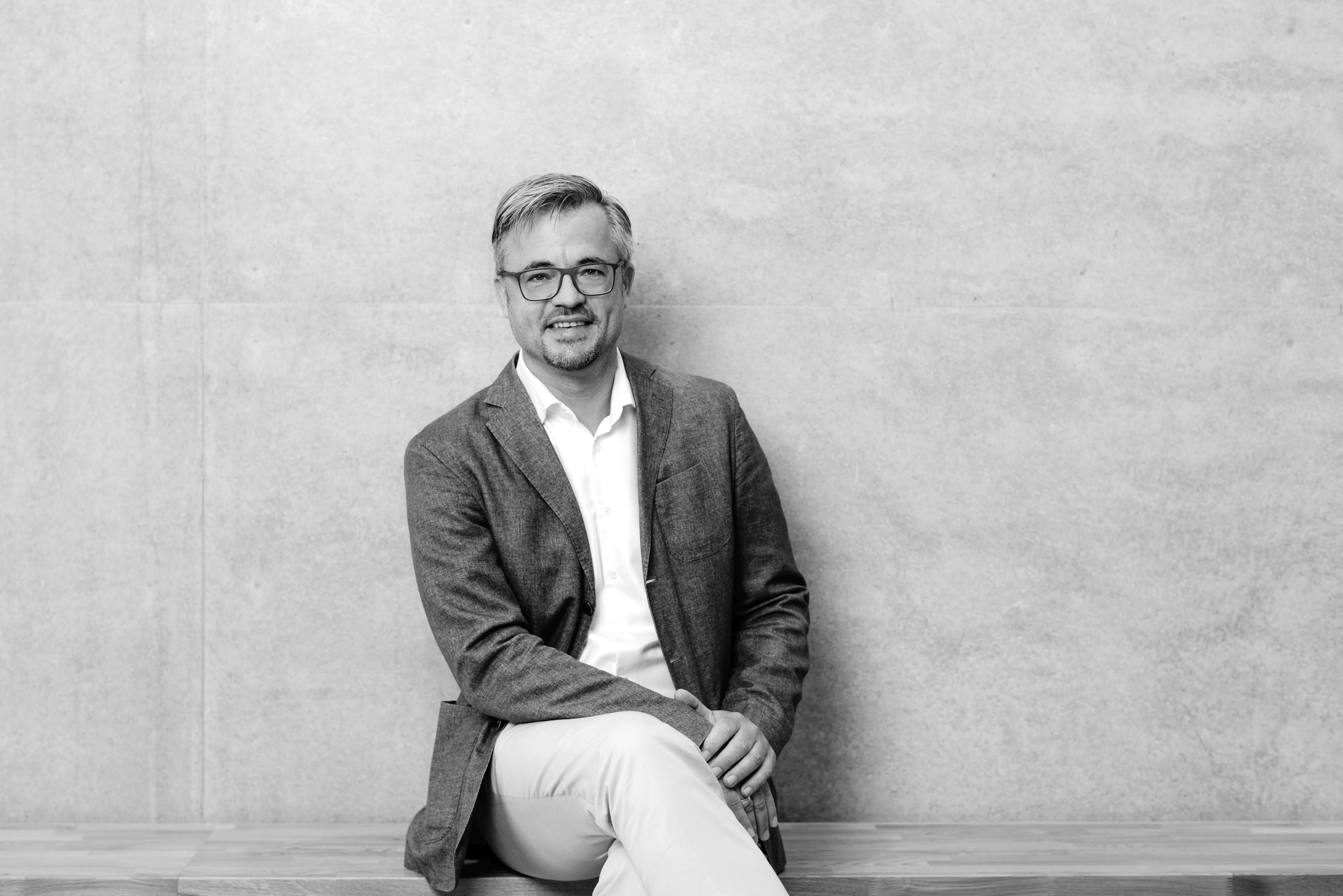 Portrait von Prof. Dr. Guido Baltes, lächelnd, mit Brille, im Sakko vor hellem Hintergrund.