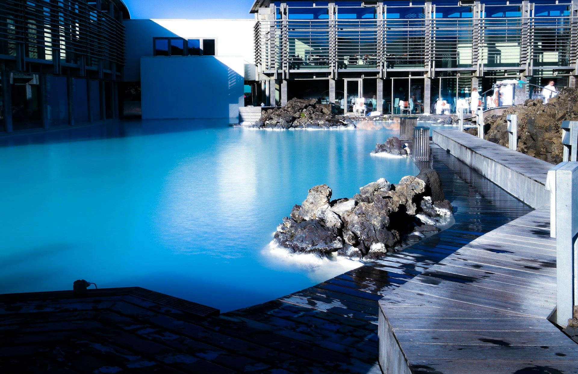 Blue Lagoon geothermal spa in Iceland with milky blue water, lava rocks, and a wooden boardwalk.&nbsp;