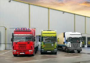 3 delivery trucks one in red, green and white is docked on a warehouse for the unloading