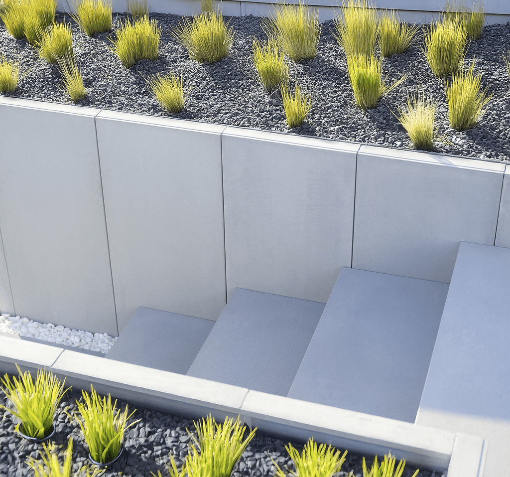 Moderní dům s velkými okny, kamennou cestičkou a upraveným trávníkem, obklopený stromy pod jasnou modrou oblohou.