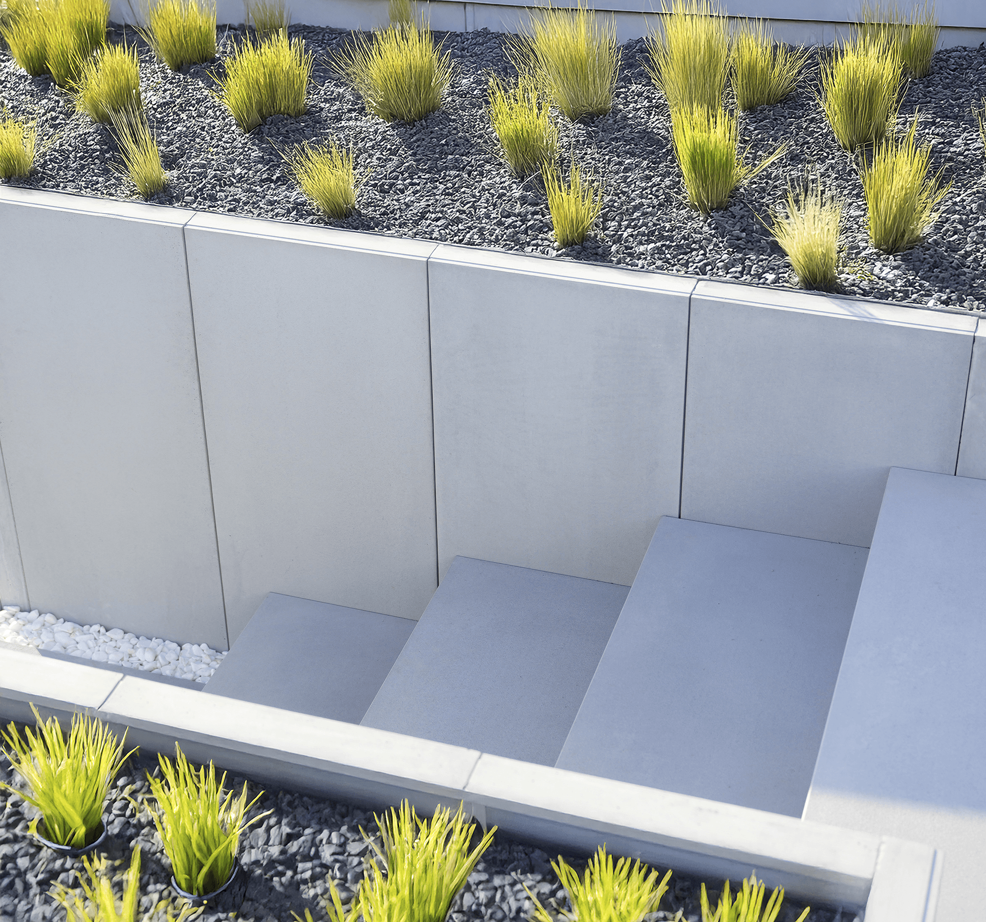 Moderní dům s velkými okny, kamennou cestičkou a upraveným trávníkem, obklopený stromy pod jasnou modrou oblohou.