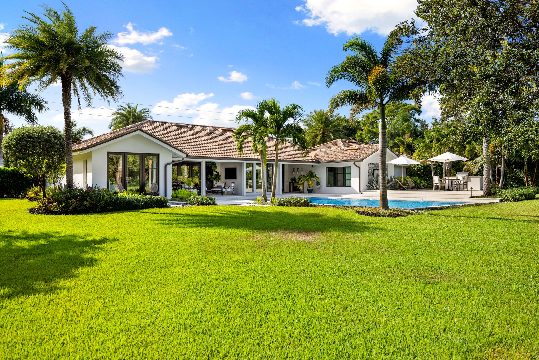 a sprawling field surrounded by palm trees with a large home in the center of the frame