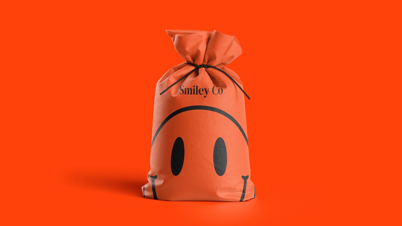 Bright orange drawstring fabric bag tied at the top, printed with a bold black smiley face and the text “Smiley Co” above it against an orange background.