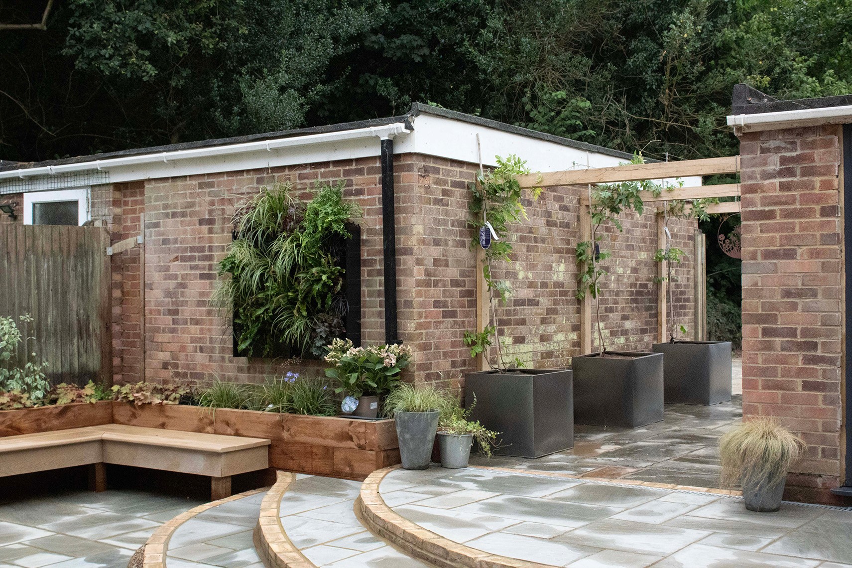 A modern outdoor space with brick walls, a patio, and surrounding greenery, featuring a shaded area.