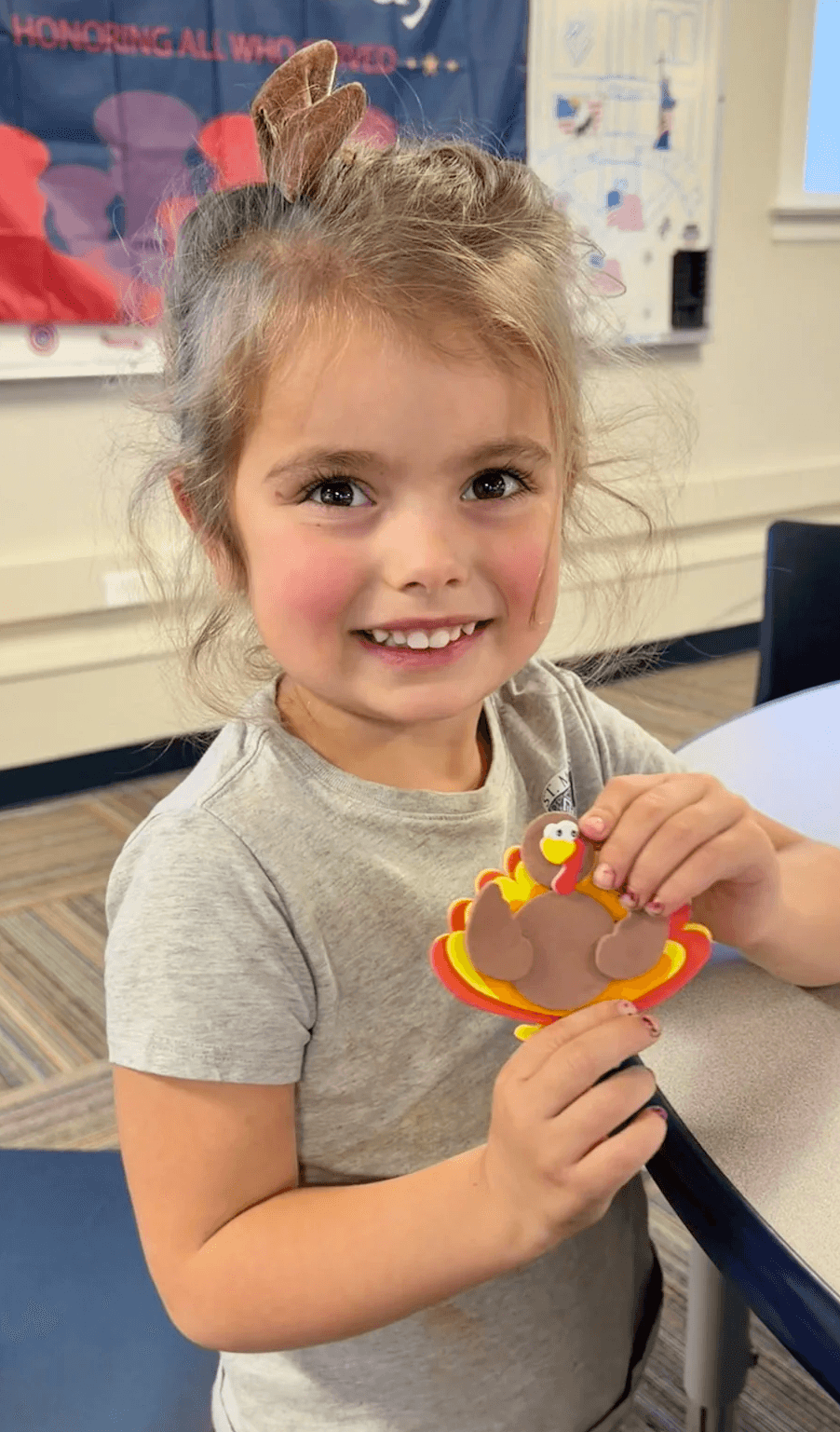 A young student holding up a paper turkey craft on Veterans Day
