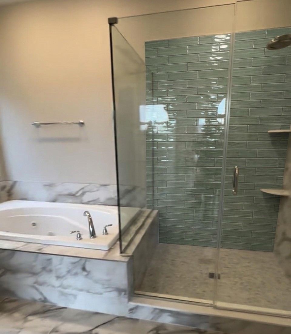 Same bathroom with sage green textured subway tile on shower walls, marble floor and tub surround preserved