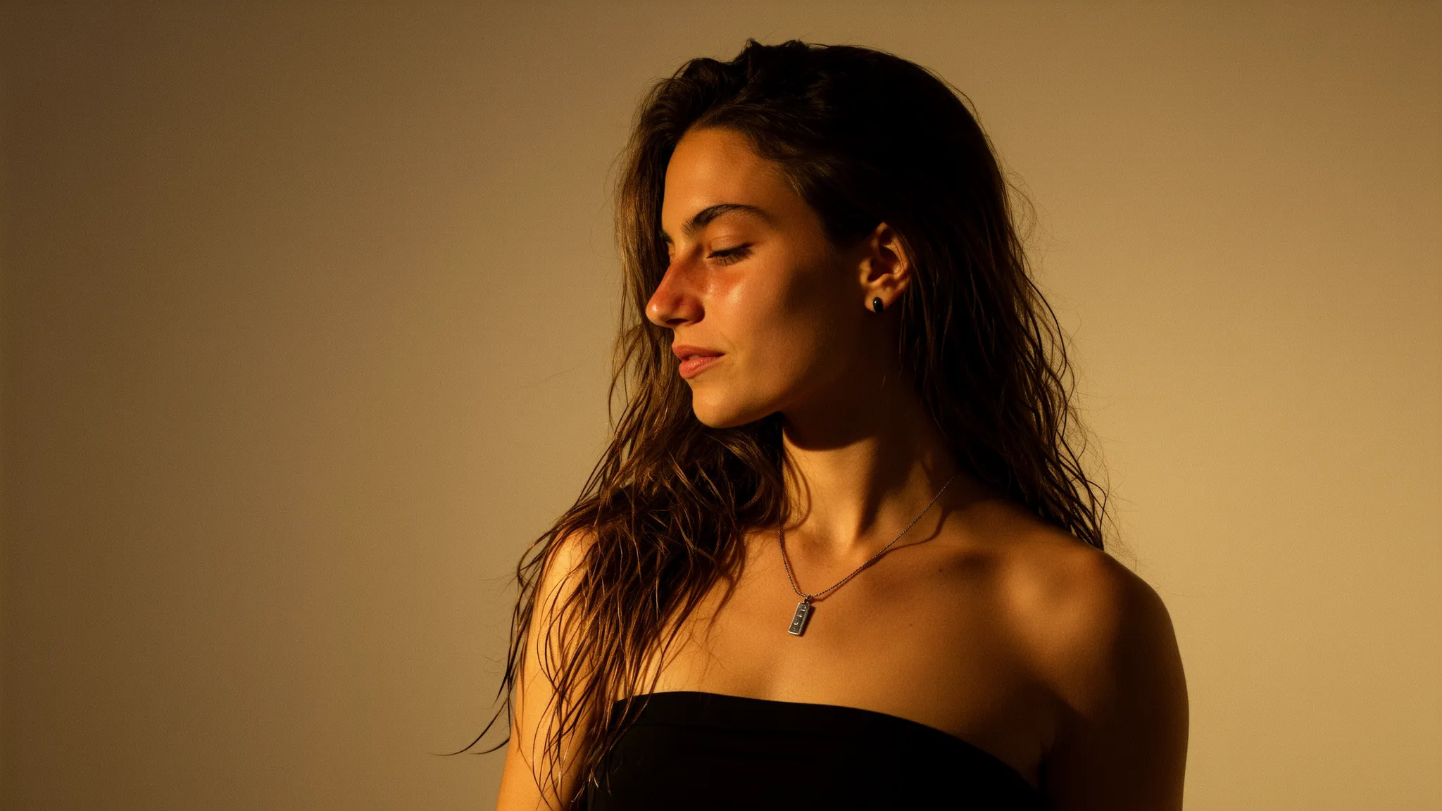 Weibliches KI-Model im warmen Seitenlicht, mit nassen welligen Haaren und schulterfreiem schwarzen Top, blickt ruhig zur Seite