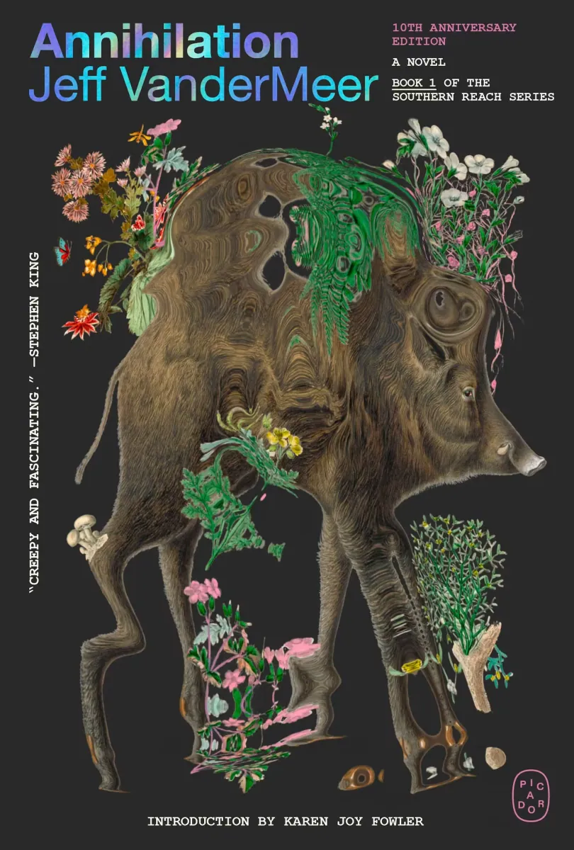 The image features the cover of "Annihilation" by Jeff VanderMeer, displaying an ornately illustrated wild boar entwined with diverse, vividly coloured plant life, set against a dark backdrop, emphasizing the book's mysterious and nature-centric theme.