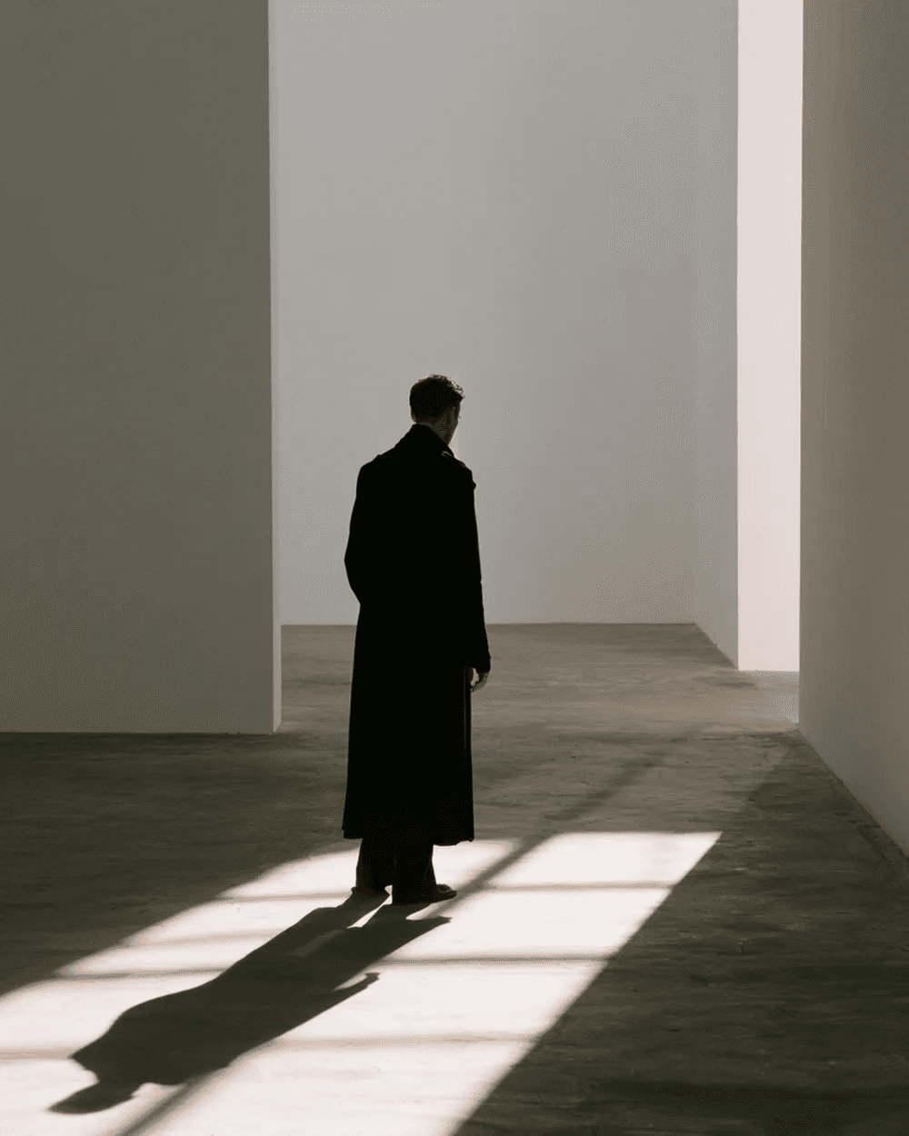 A figure in a long coat in a white room