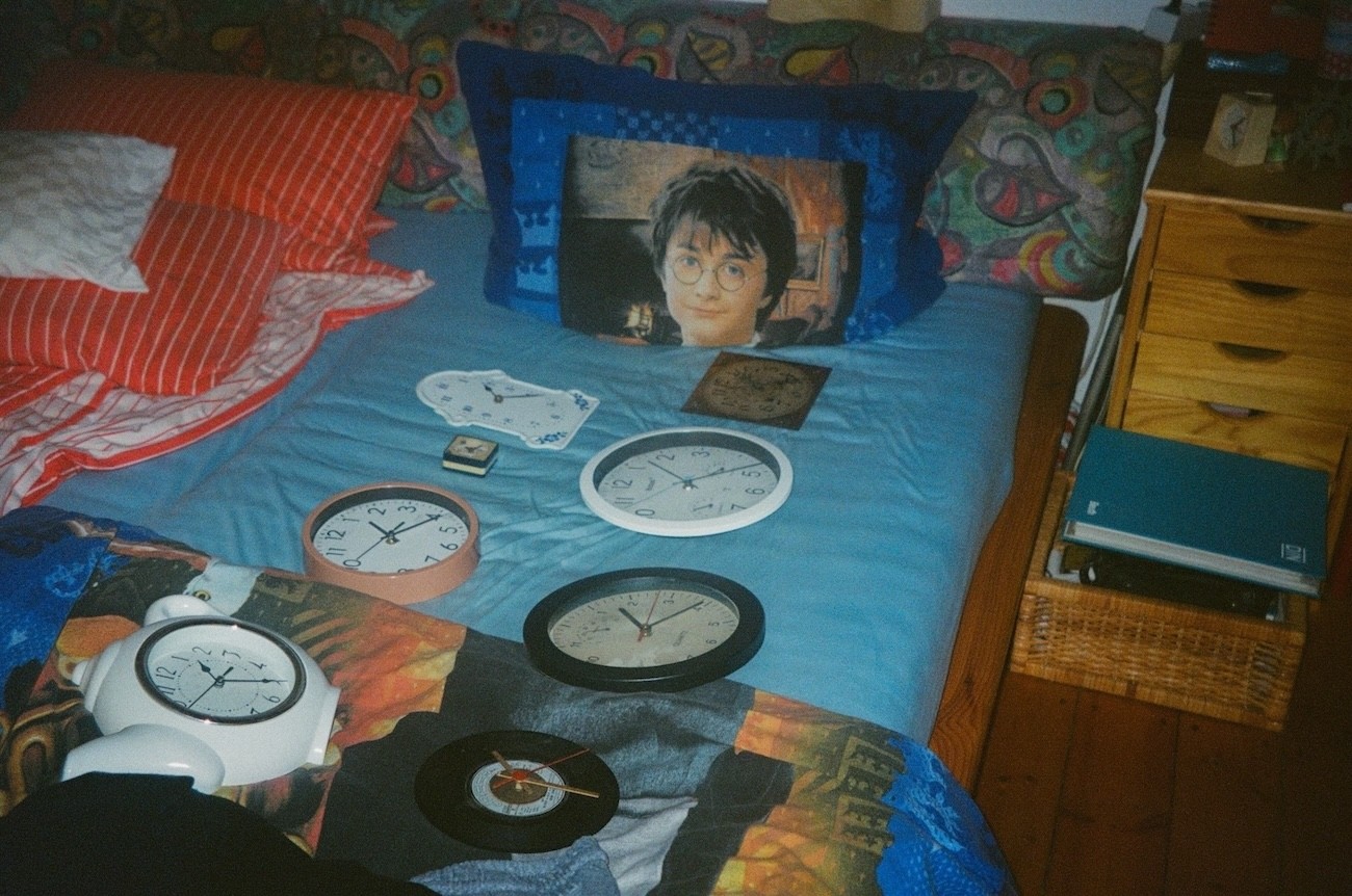 Surreal scene with multiple clocks on a bed next to a Harry Potter pillow