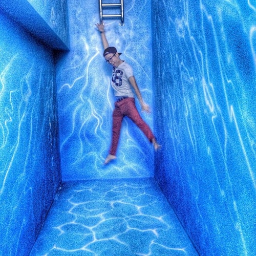 一个穿红色裤子和白色衬衫的人挂在带有水纹图案的蓝色墙壁上的梯子上。