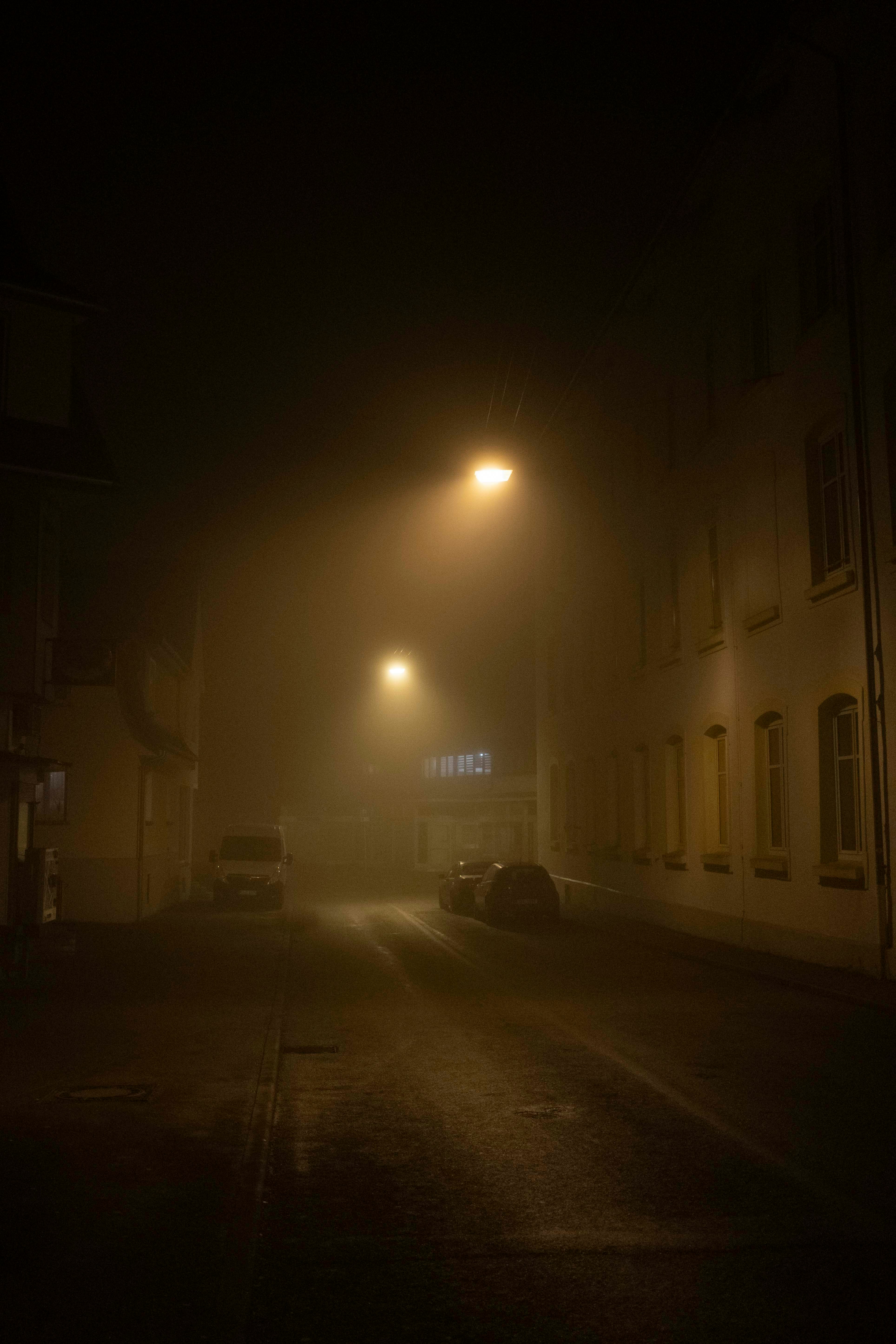 a foggy street at night with cars parked on the side of the road