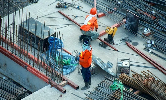 Construction workers wearing safety gear working with steel bars on a building site.