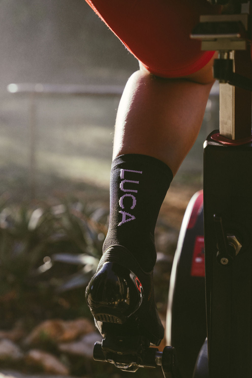 Close-up-shot-of-a-cyclist-leg-and-foot-during-a-ride-highlighting-the-black-Luca-cycling-socks-with-the-vertical-purple-Luca-logo-on-the-calf
