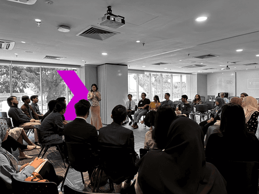 A diverse group of individuals seated in chairs, engaged in a collaborative learning environment led by an instructor.