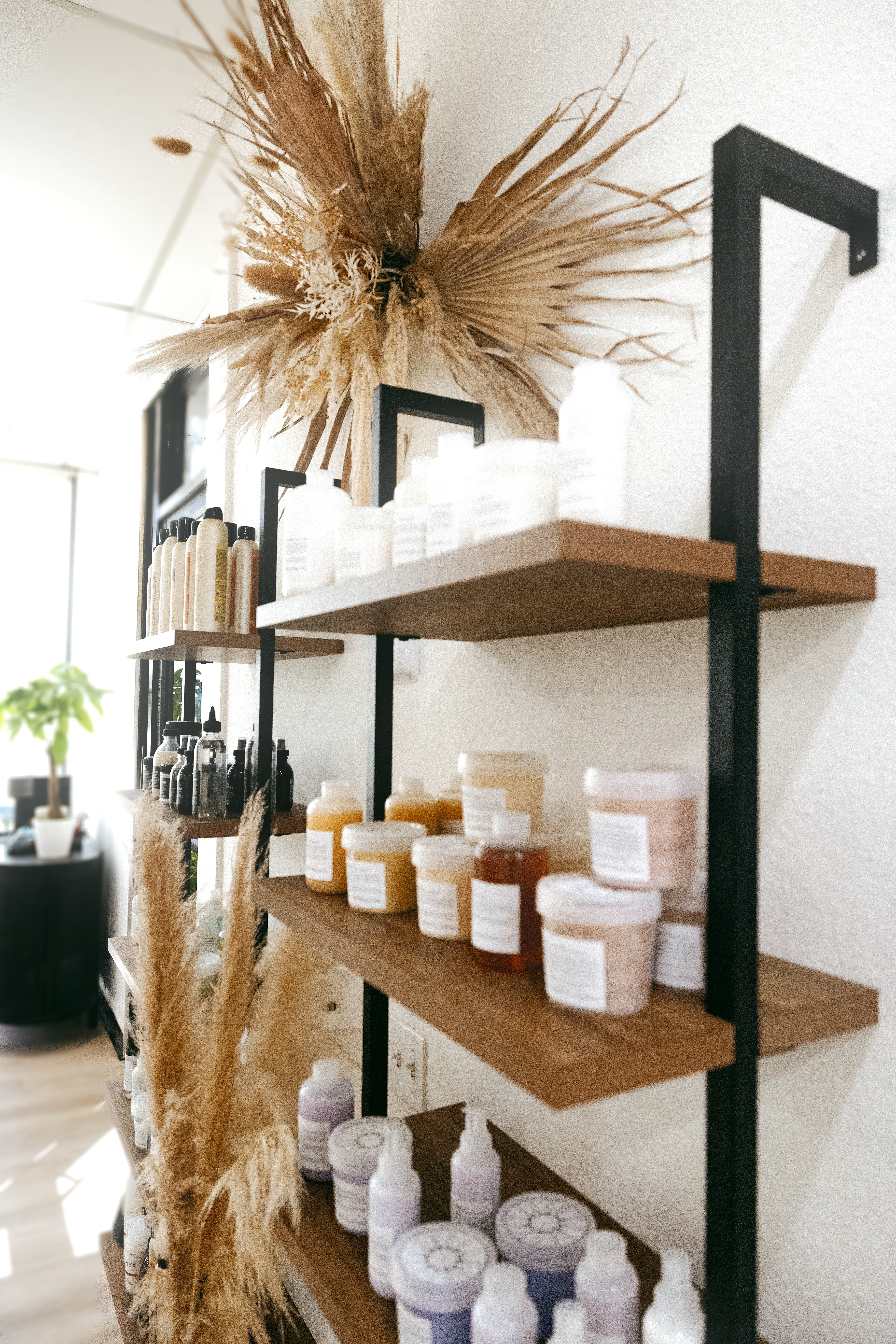 A serene and elegant spa space with wooden reclining chairs and white cushions. Golden sunlight filters through a cascading water feature, creating a peaceful atmosphere. Tropical plants and candles add to the relaxing ambiance.