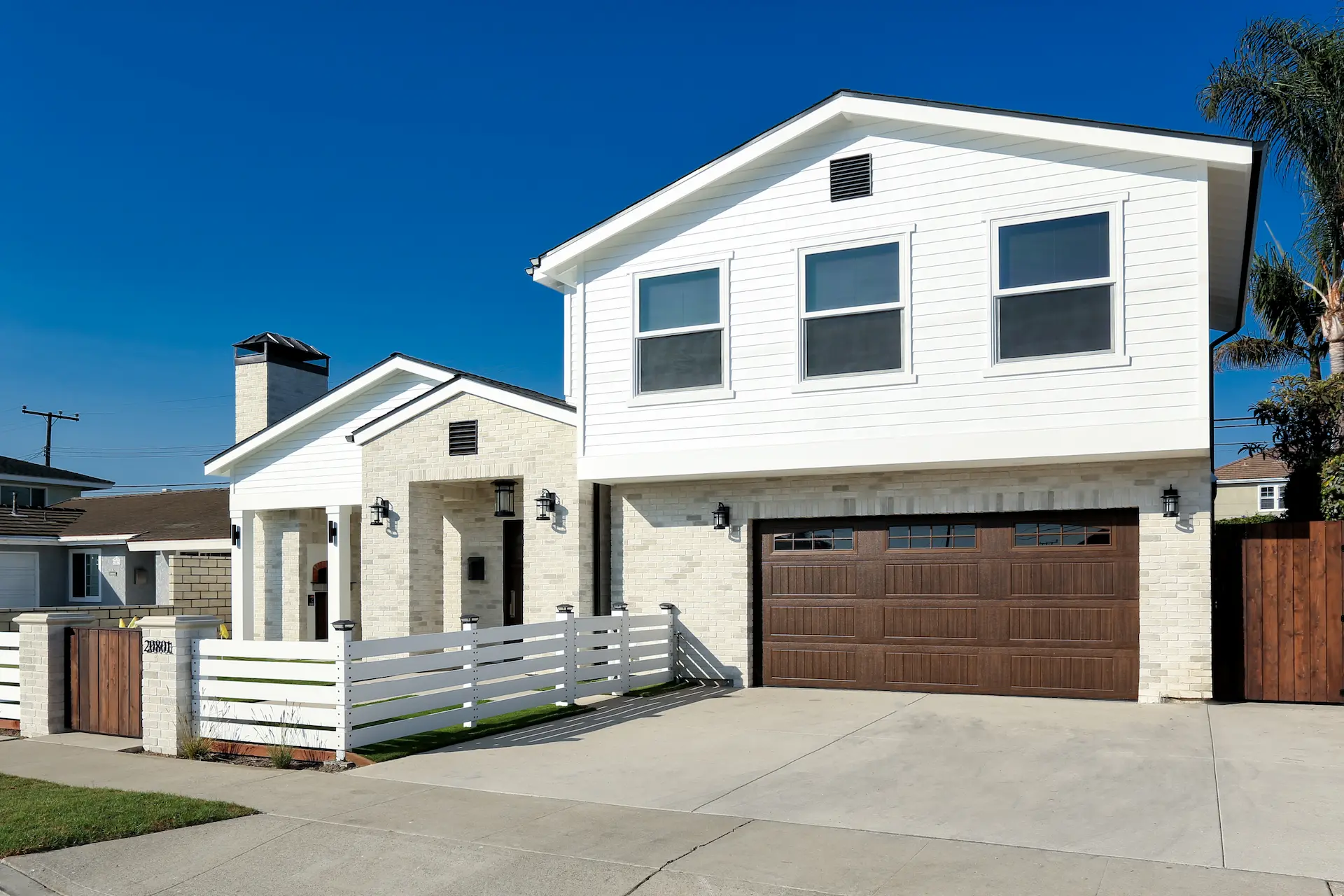 Angled front view of American Farmhouse home with white siding and brown garage door. Photo by Chris Darnall.