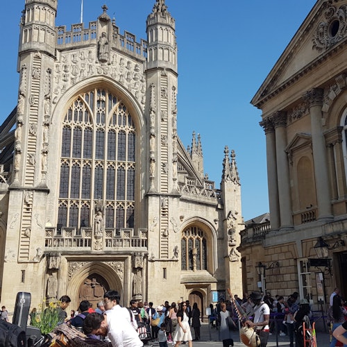 一群人在一座大型华美的哥特式建筑前聚集,建筑有高大的窗户和精美的石雕。