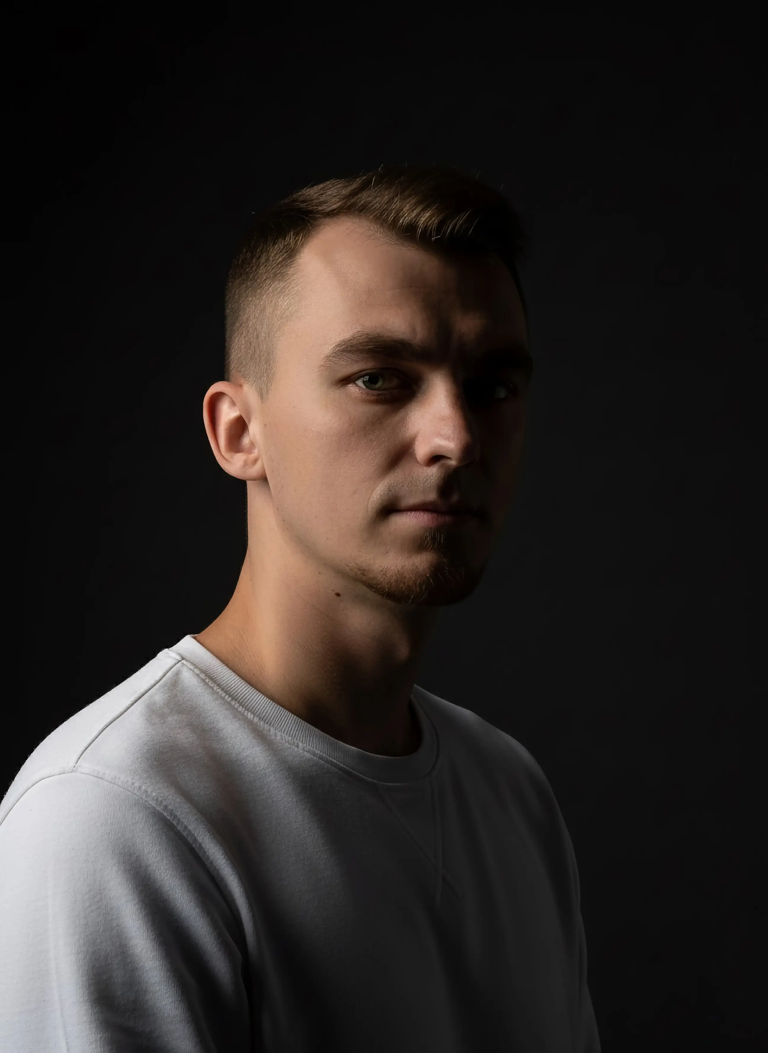 Portrait of a young man with short brown hair, wearing a white sweater, looking directly at the camera.